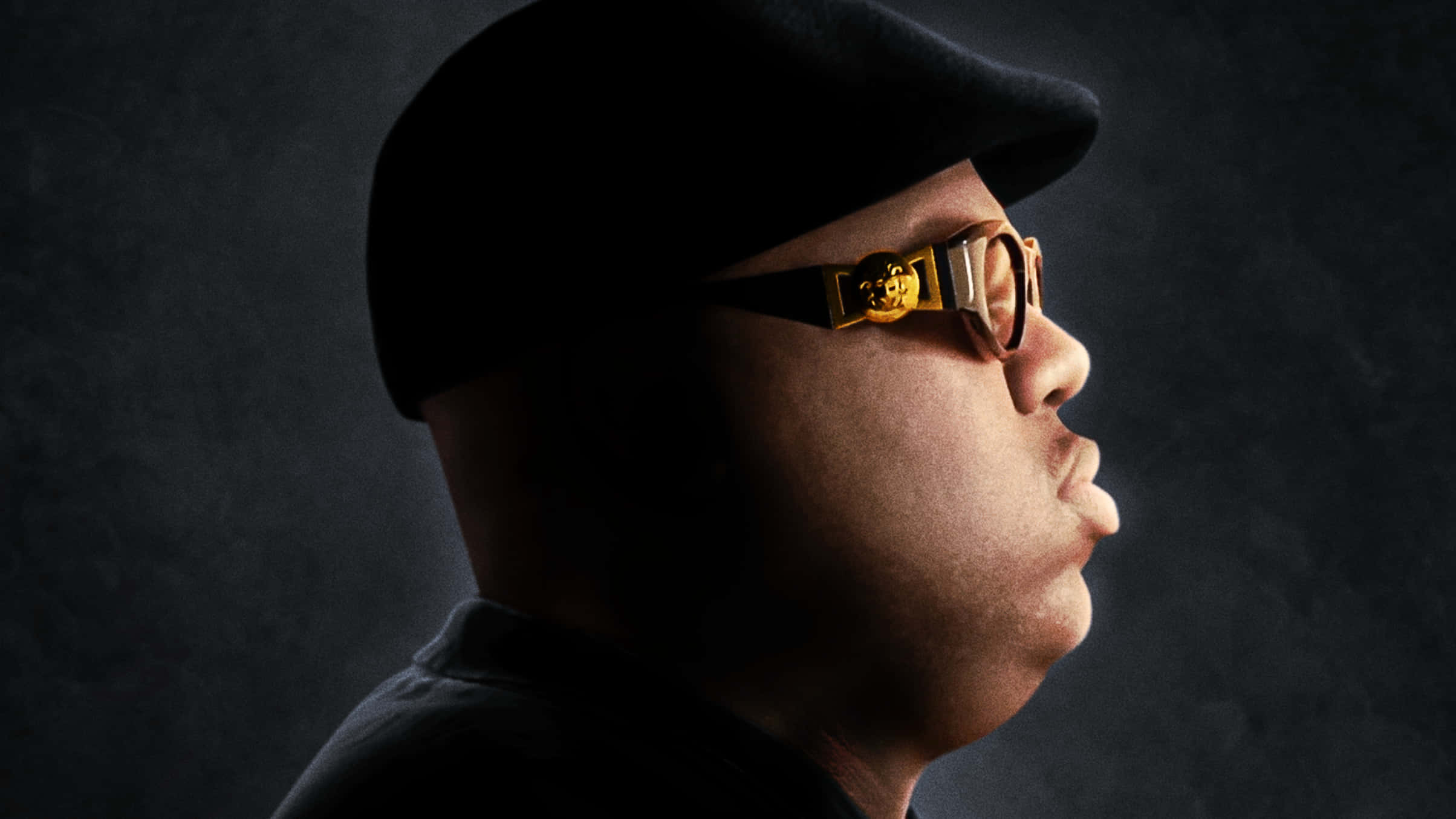 hiphop 桌布 壁紙 — 一名戴著黑色帽子和金色邊框眼鏡的男性側面，背景為深色紋理。