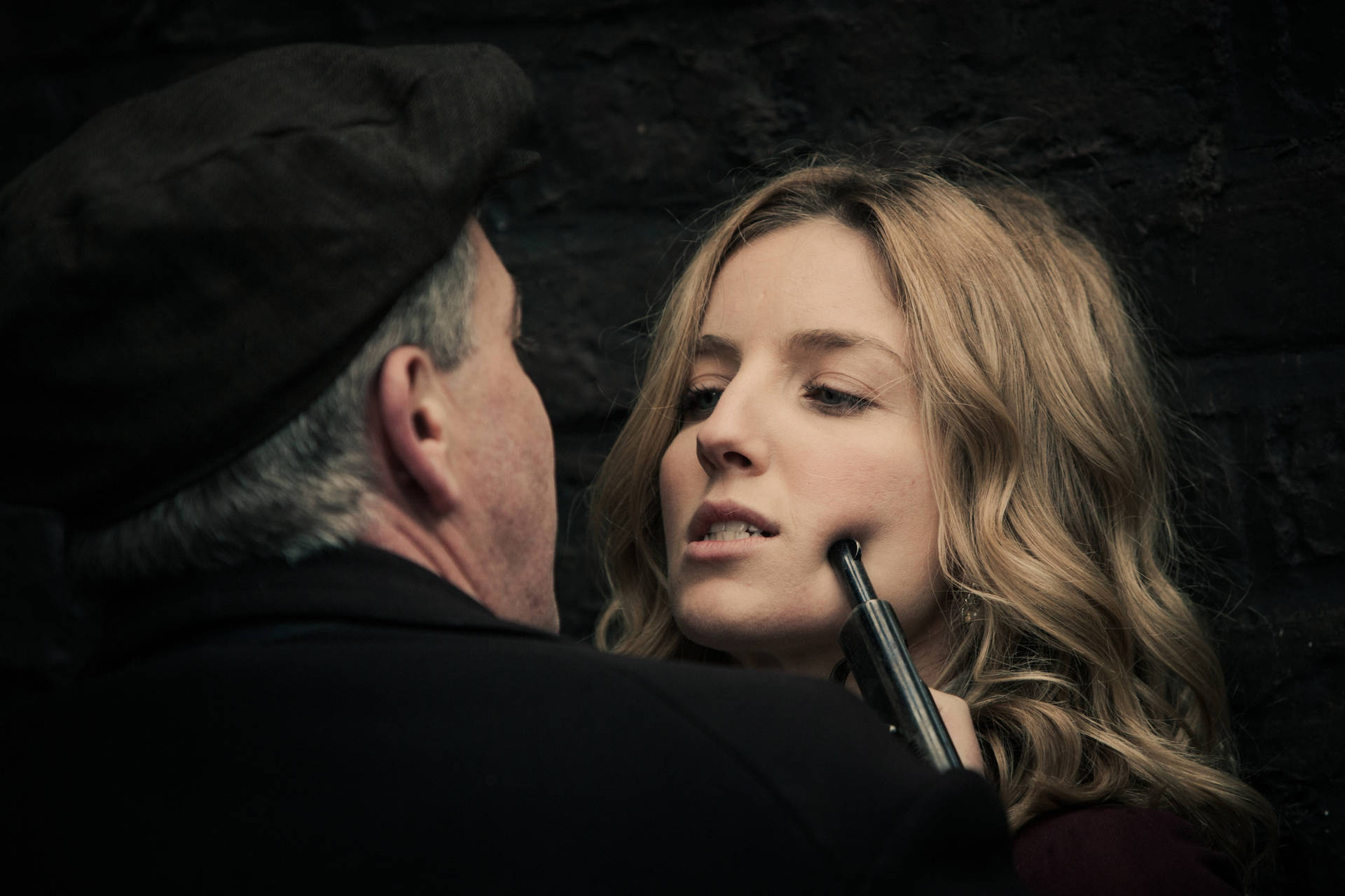男子在黑暗磚牆房間內用槍抵住女子下巴。 — Peaky Blinders 壁紙