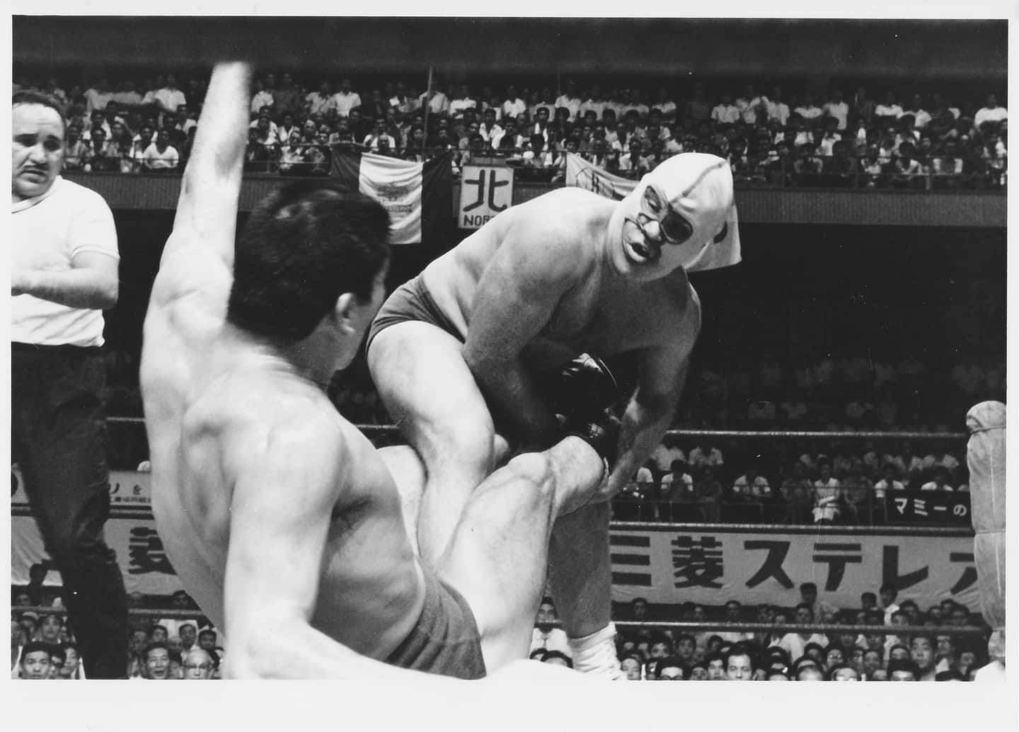 WWE 桌布 壁紙 — 一名戴面具的摔角手在擠滿觀眾的競技場中，戲劇性地舉起對手。