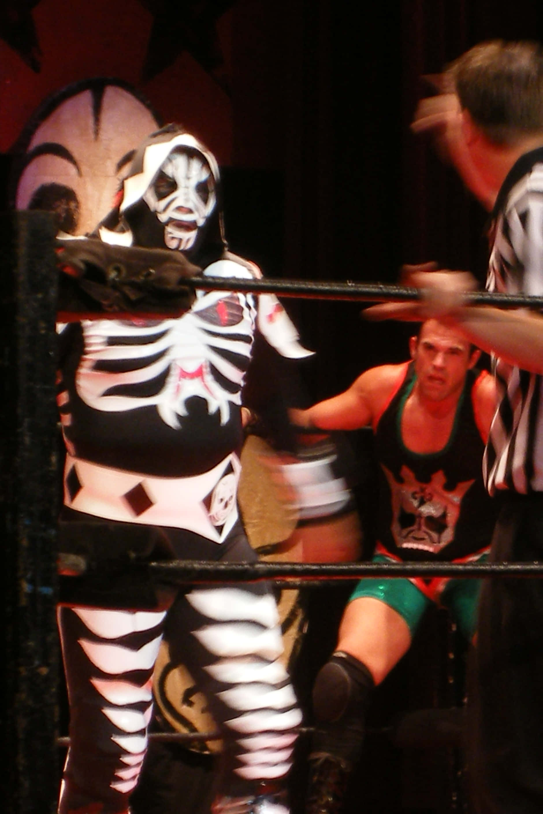 La Parka 桌布 壁紙 — 一名戴面具的摔角手穿著黑白骷髏服裝，在明亮的燈光下於摔角場內與對手搏鬥。