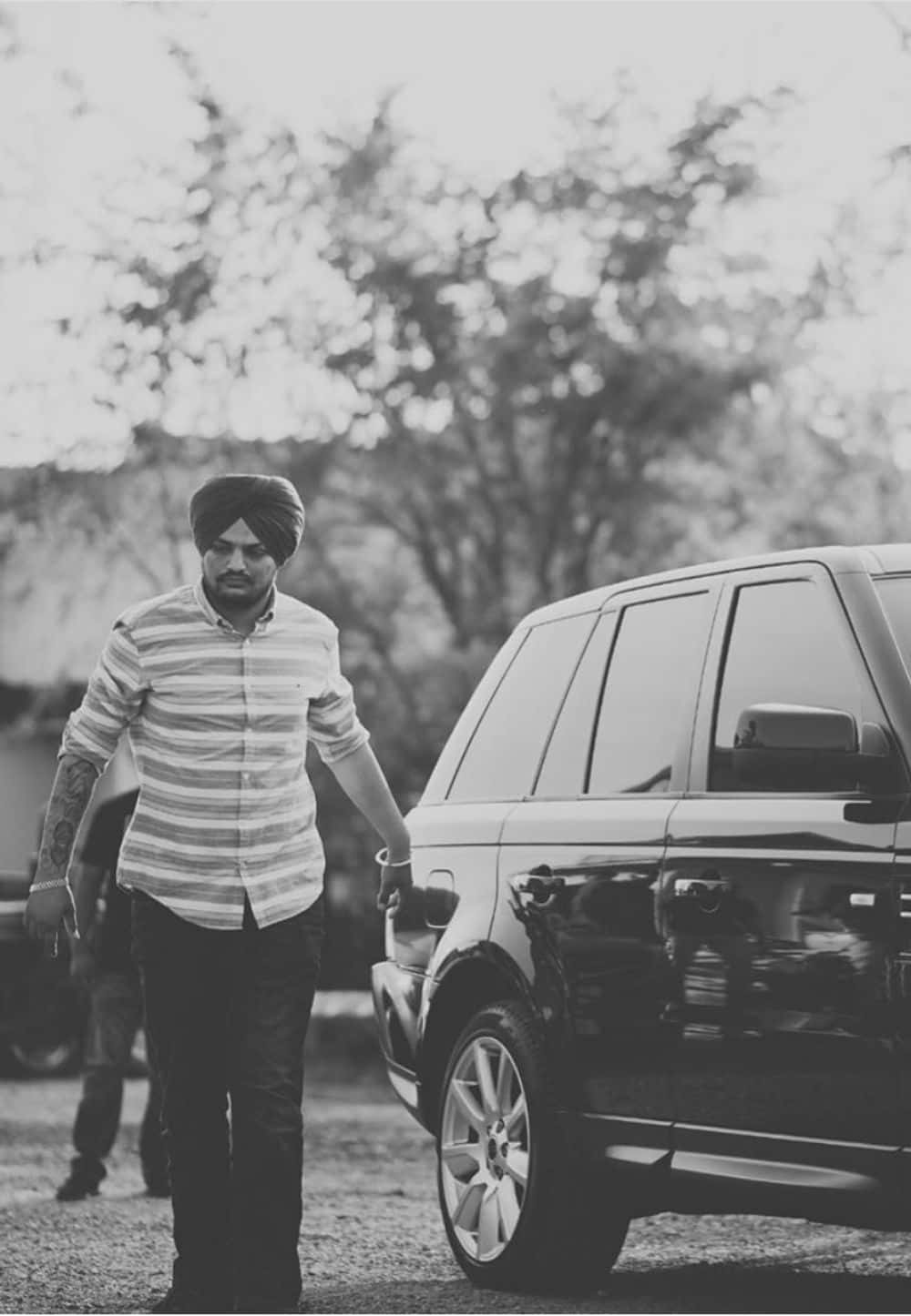 戴頭巾的男子在戶外走在一輛黑色SUV旁邊。 — Sidhu Moose Wala 壁紙