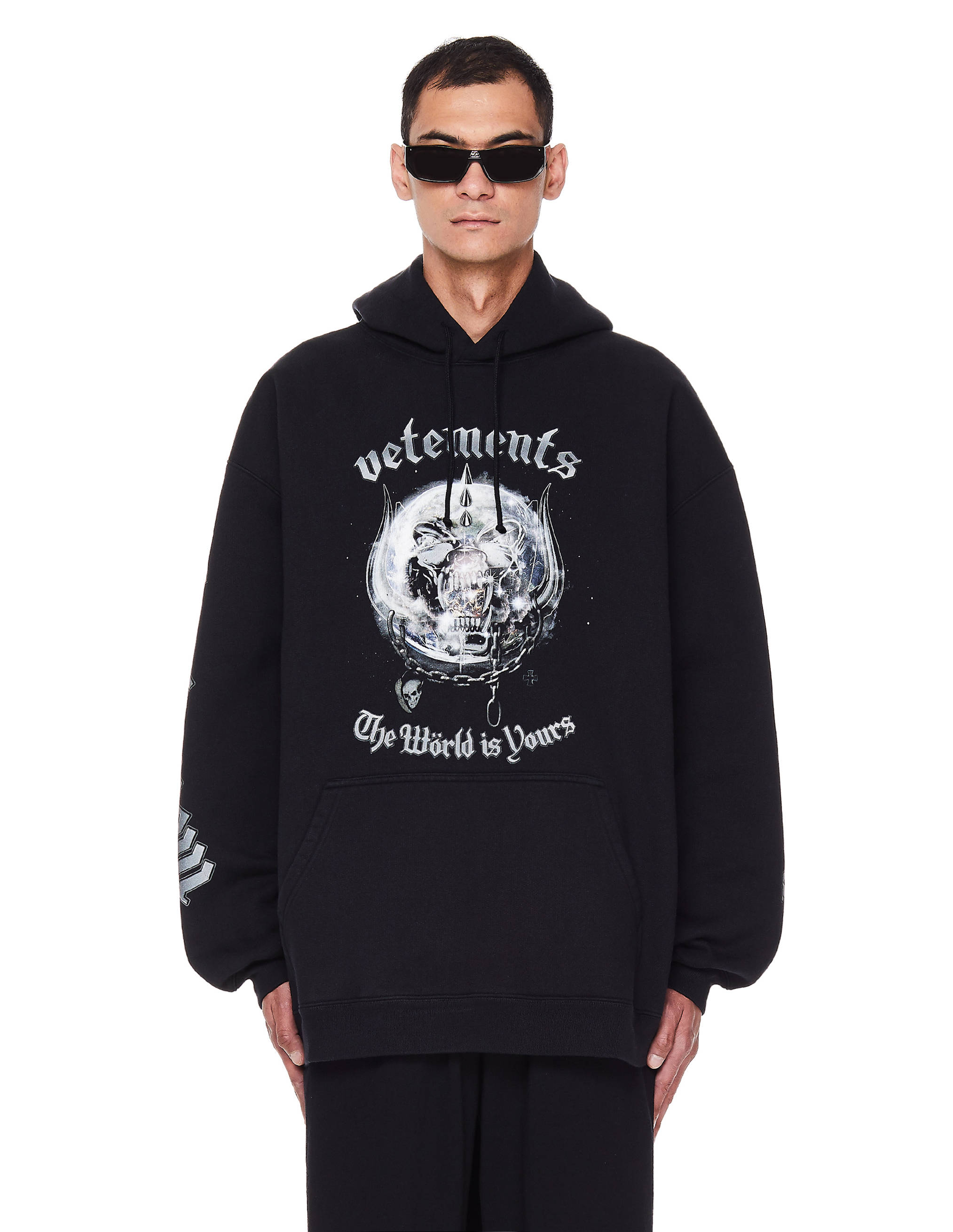 vetements 桌布 壁紙 — 一名戴黑色太陽眼鏡的男子，身穿印有骷髏圖案和文字「Vetements The World is Yours」的 oversized 黑色連帽衫，背景為白色。