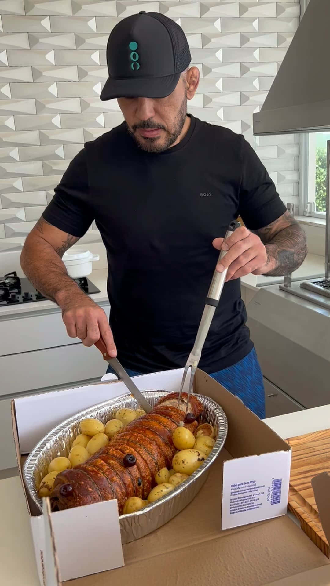 UFC 桌布 壁紙 — 一名戴黑色帽子和穿黑色襯衫的男子在現代廚房裡切著被馬鈴薯包圍的烤釀豬腰肉。