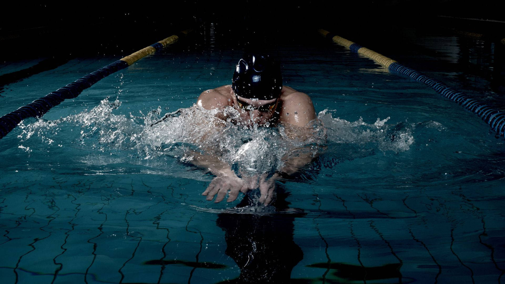 Swimming 桌布 壁紙 — 一名戴黑色泳帽的泳者在戲劇性燈光下強力划過深藍色泳池水。