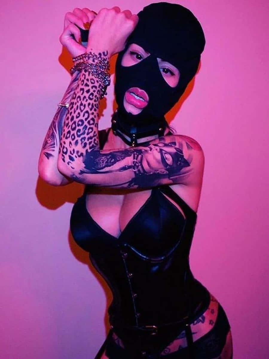 Ski Mask Girl 桌布 壁紙 — 一名戴黑色頭套、穿緊身胸衣的女性，在鮮豔的粉紅色牆壁前展示有刺青的手臂擺姿勢。