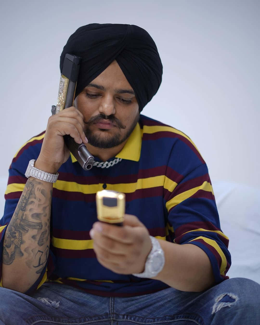 戴頭巾男子手持金色手機，同時看著另一支手機 — Sidhu Moose Wala 壁紙