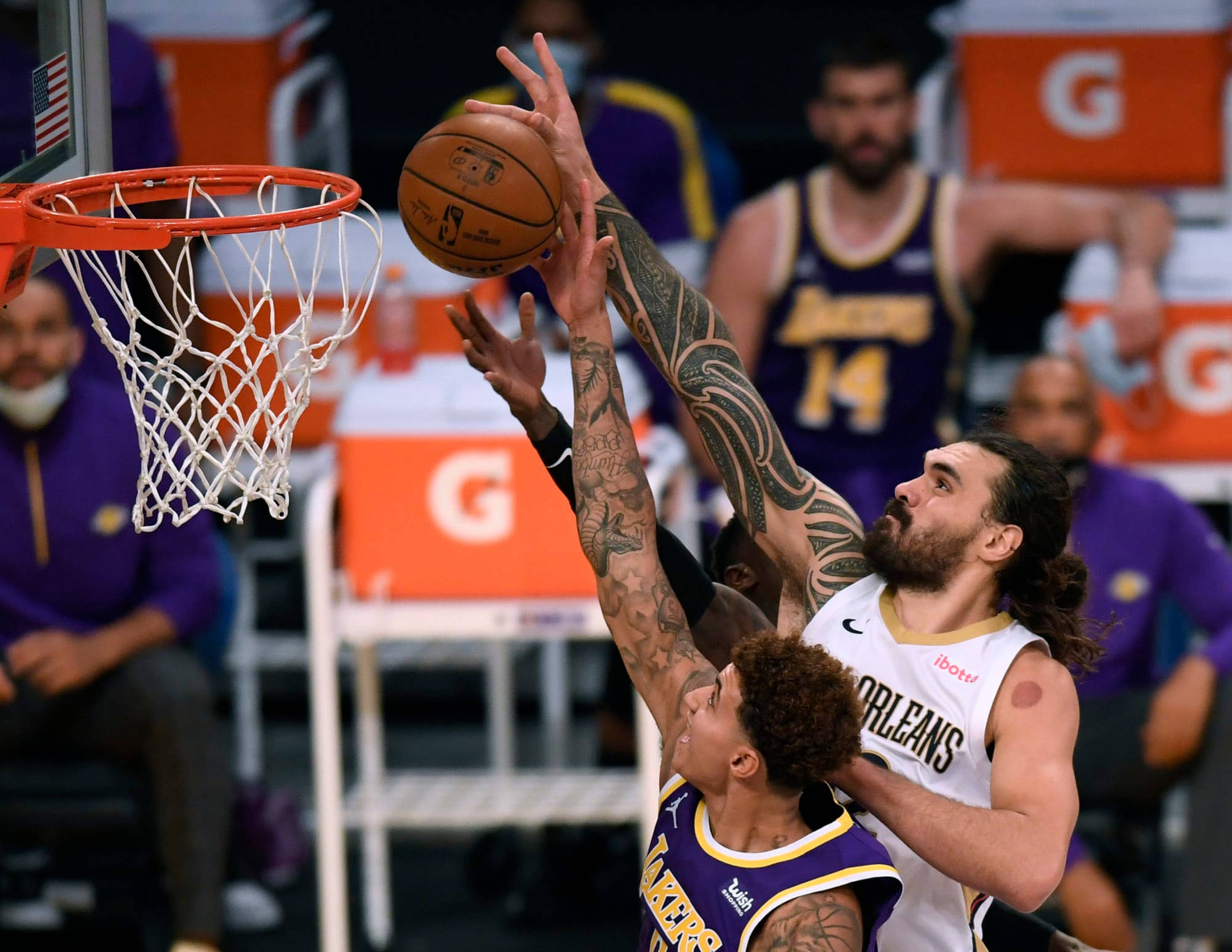 Steven Adams 桌布 壁紙 — 一名手臂有刺青的籃球運動員在明亮的場館燈光下跳起灌籃，防守球員試圖封阻投籃。