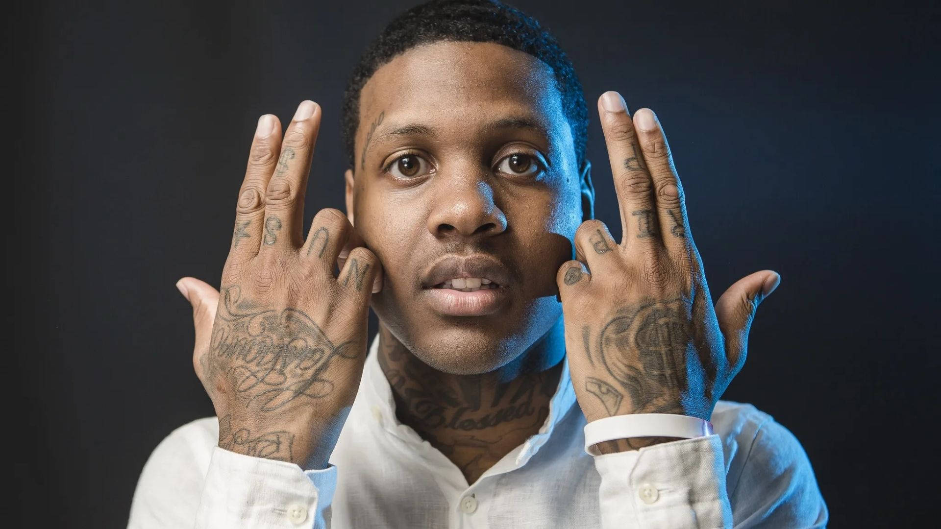 Lil Durk 桌布 壁紙 — 一名手部和頸部有刺青的男子在深色背景下，在冷藍色燈光下強烈擺姿勢。