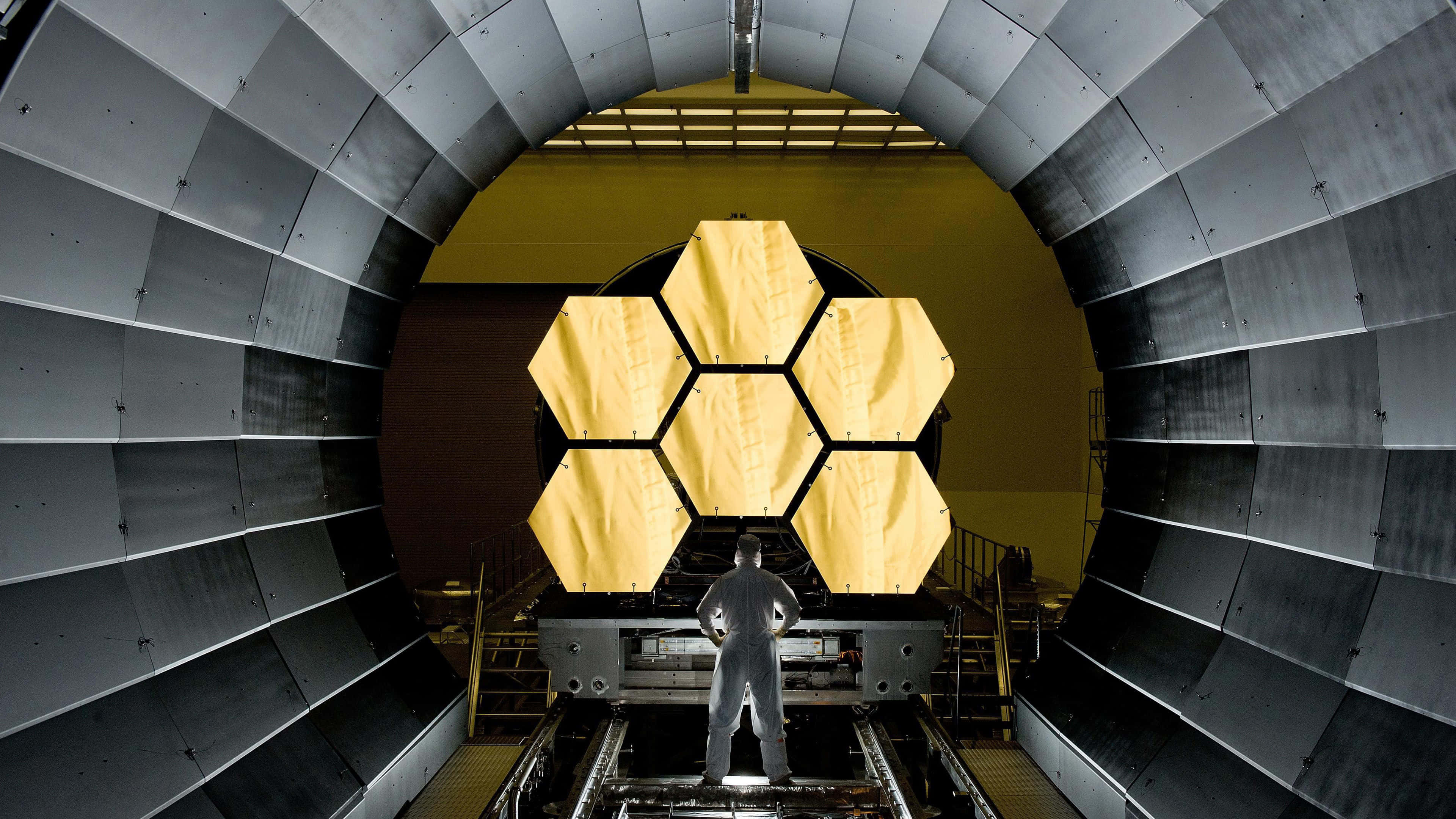 Telescope 桌布 壁紙 — 一名技術人員站在巨大的金屬無塵室內，面對詹姆斯·韋伯太空望遠鏡的金色六角形鏡面分段。