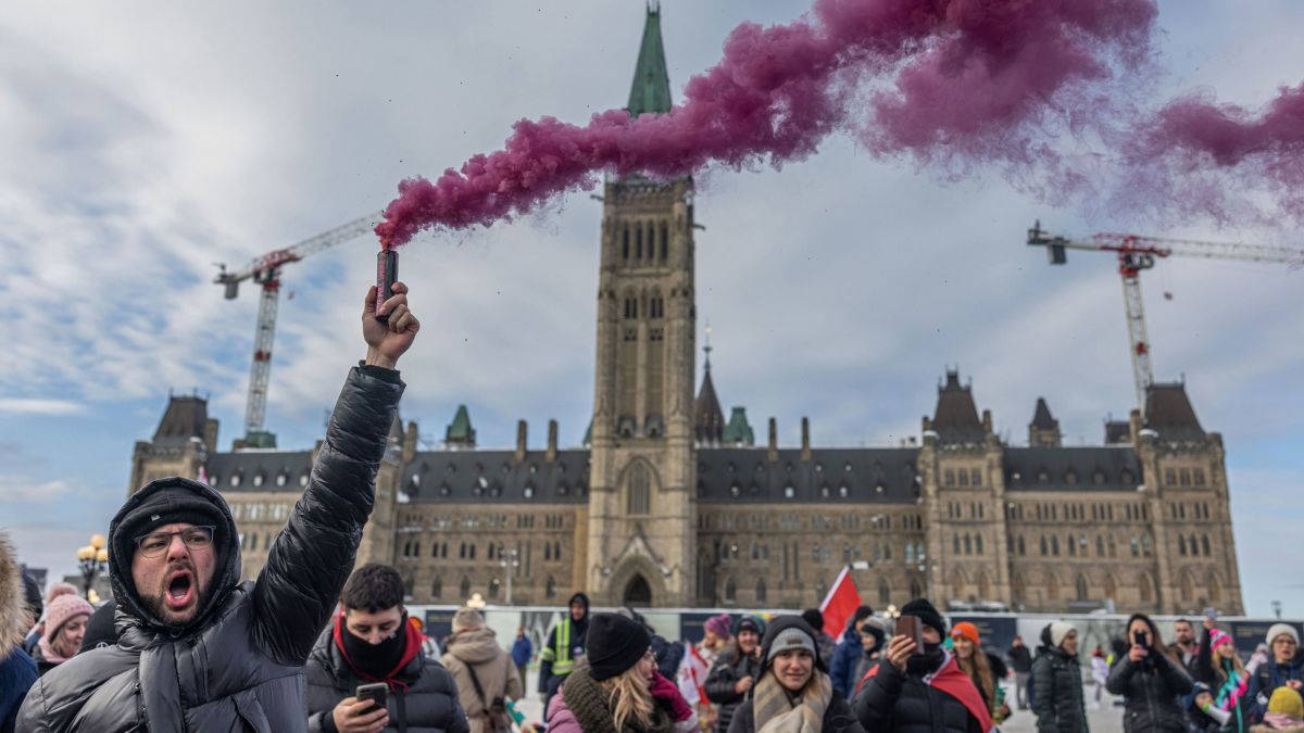 Canadian 桌布 壁紙 — 一名抗議者在多雲的天空下，在加拿大國會大廈前高舉紫色煙霧信號彈。