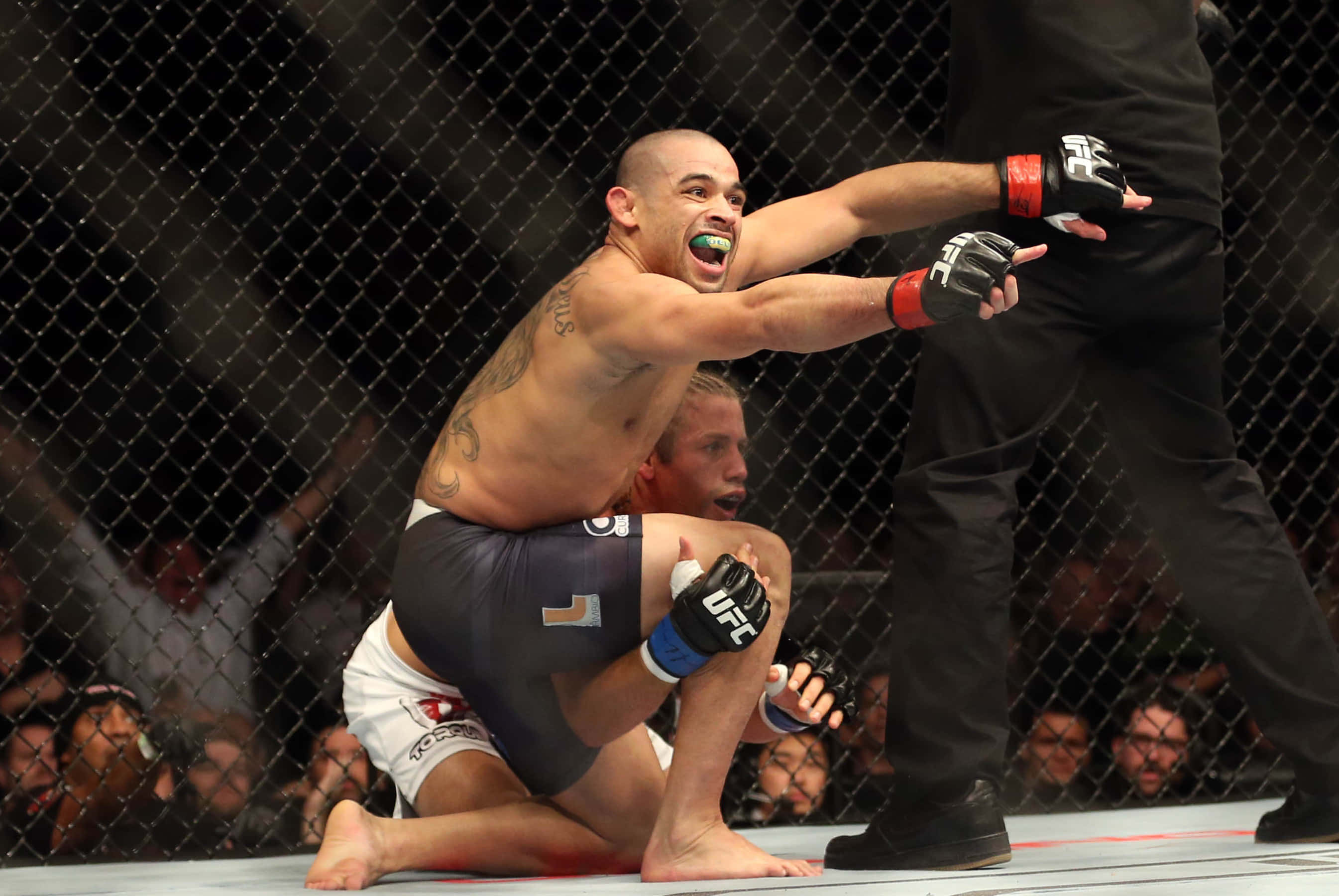 UFC 桌布 壁紙 — 一名拳手在UFC八角籠中高舉雙臂慶祝勝利，裁判介入終止比賽。