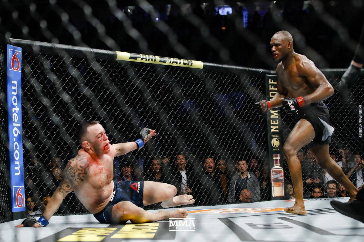 UFC 桌布 壁紙 — 一名拳手在八角籠地上倒下，而他的對手在明亮的場館燈光下於UFC比賽中勝利站立。