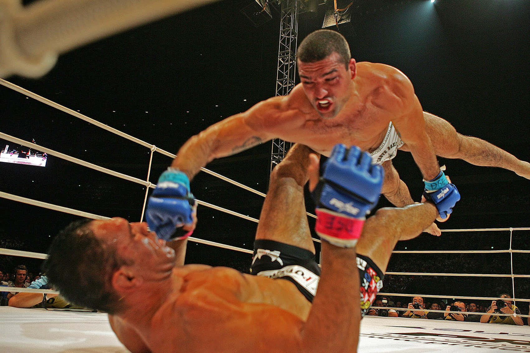 Champion 桌布 壁紙 — 一名拳手在明亮的MMA擂台上，於場館燈光下對對手使出飛膝攻擊。