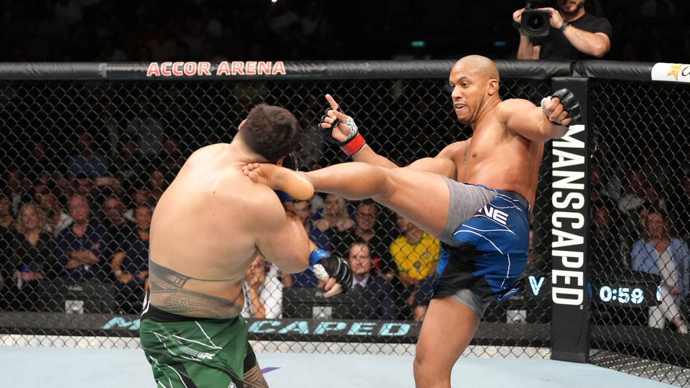 MMA 桌布 壁紙 — 一名拳手在明亮的場館燈光下，於UFC八角籠中向對手使出高踢。