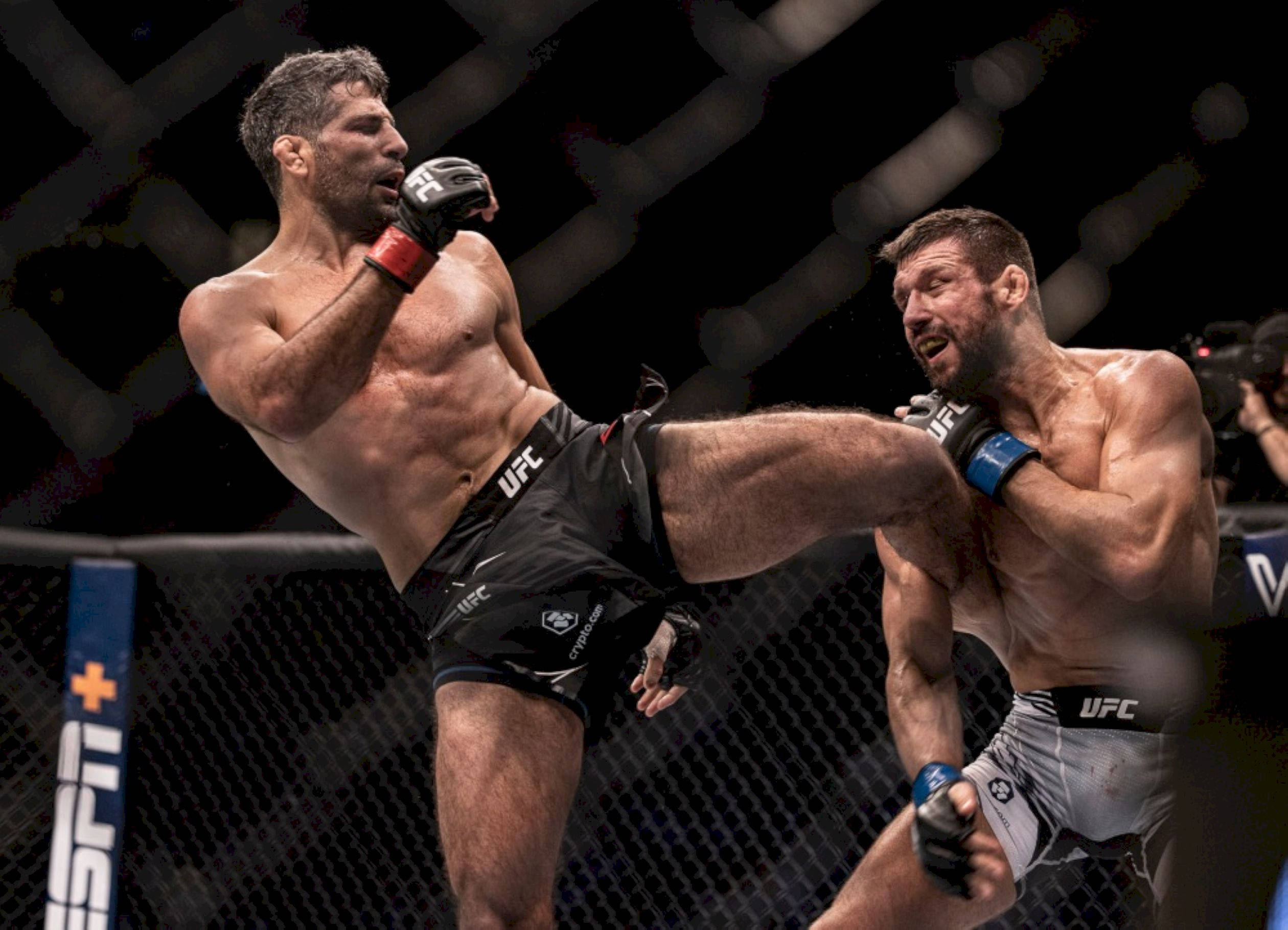MMA 桌布 壁紙 — 一名拳手在明亮的場館燈光下，於UFC八角籠中向對手使出高踢。