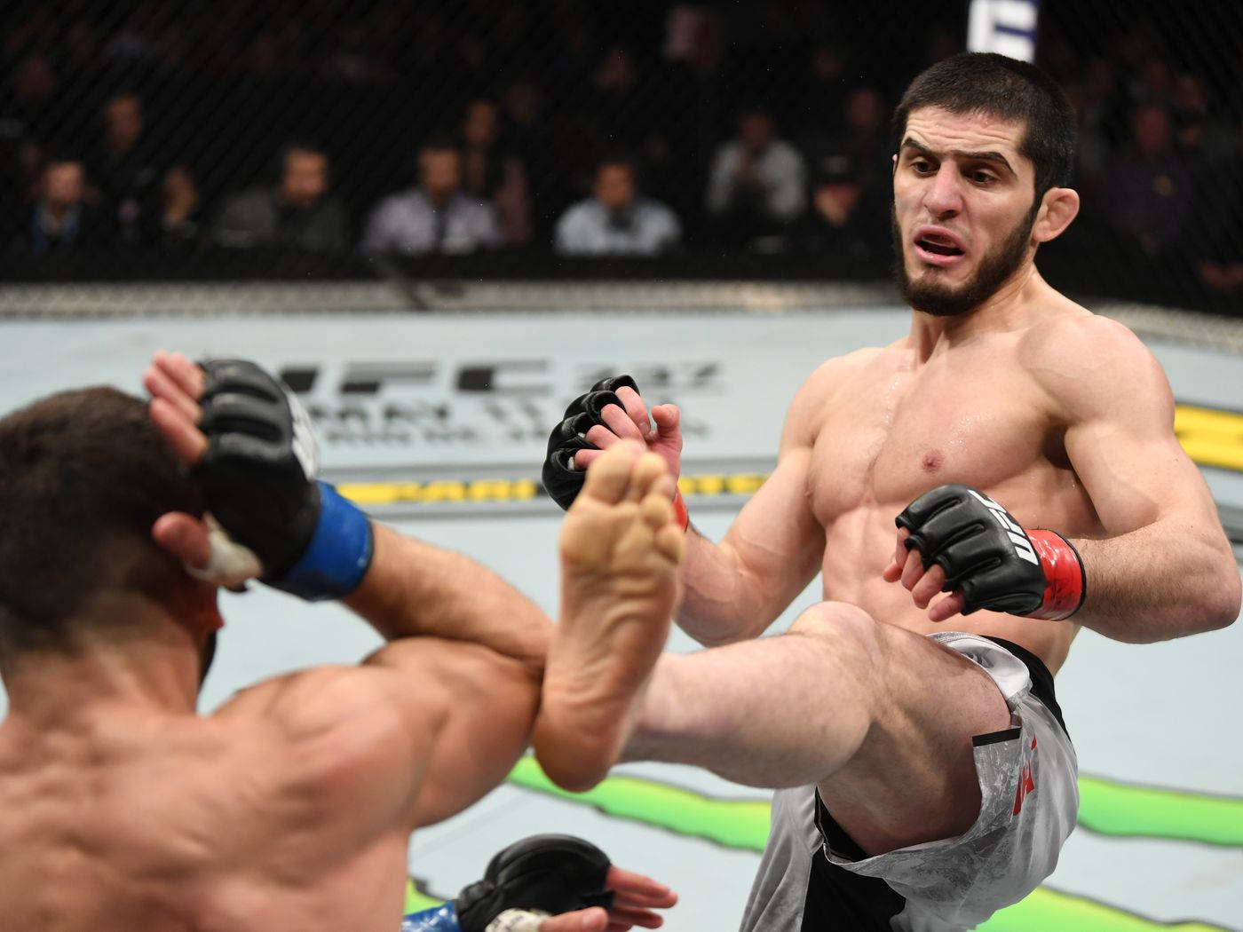 UFC 桌布 壁紙 — 一名拳手在明亮的場館燈光下，於UFC八角籠中向對手使出高踢。