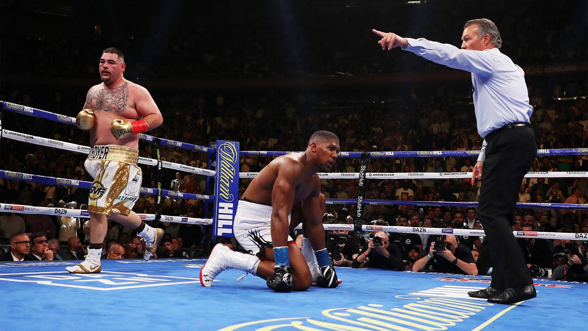 Anthony Joshua 桌布 壁紙 — 一名拳擊手在擂台上跪地敗陣，對手勝利站立，裁判指向結束比賽。