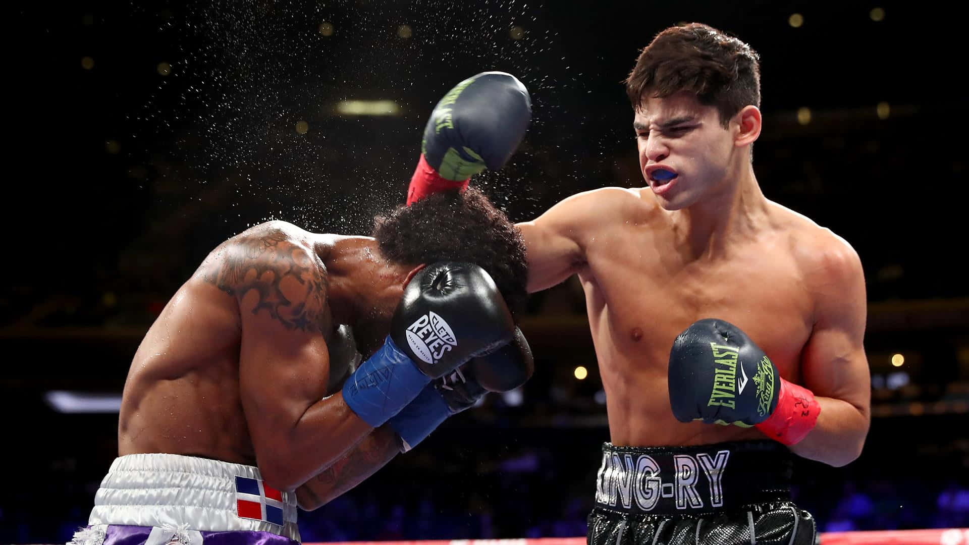Ryan Garcia 桌布 壁紙 — 一名拳擊手在燈光明亮的擂台上向對手打出強勁的右勾拳，汗水在空中飛濺。