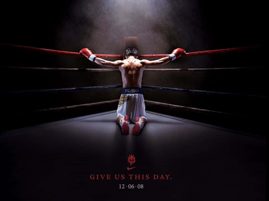 Boxing 桌布 壁紙 — 一名拳擊手在燈光昏暗的擂台上跪下，雙臂高舉抓住繩索，聚光燈從上方照射下來。
