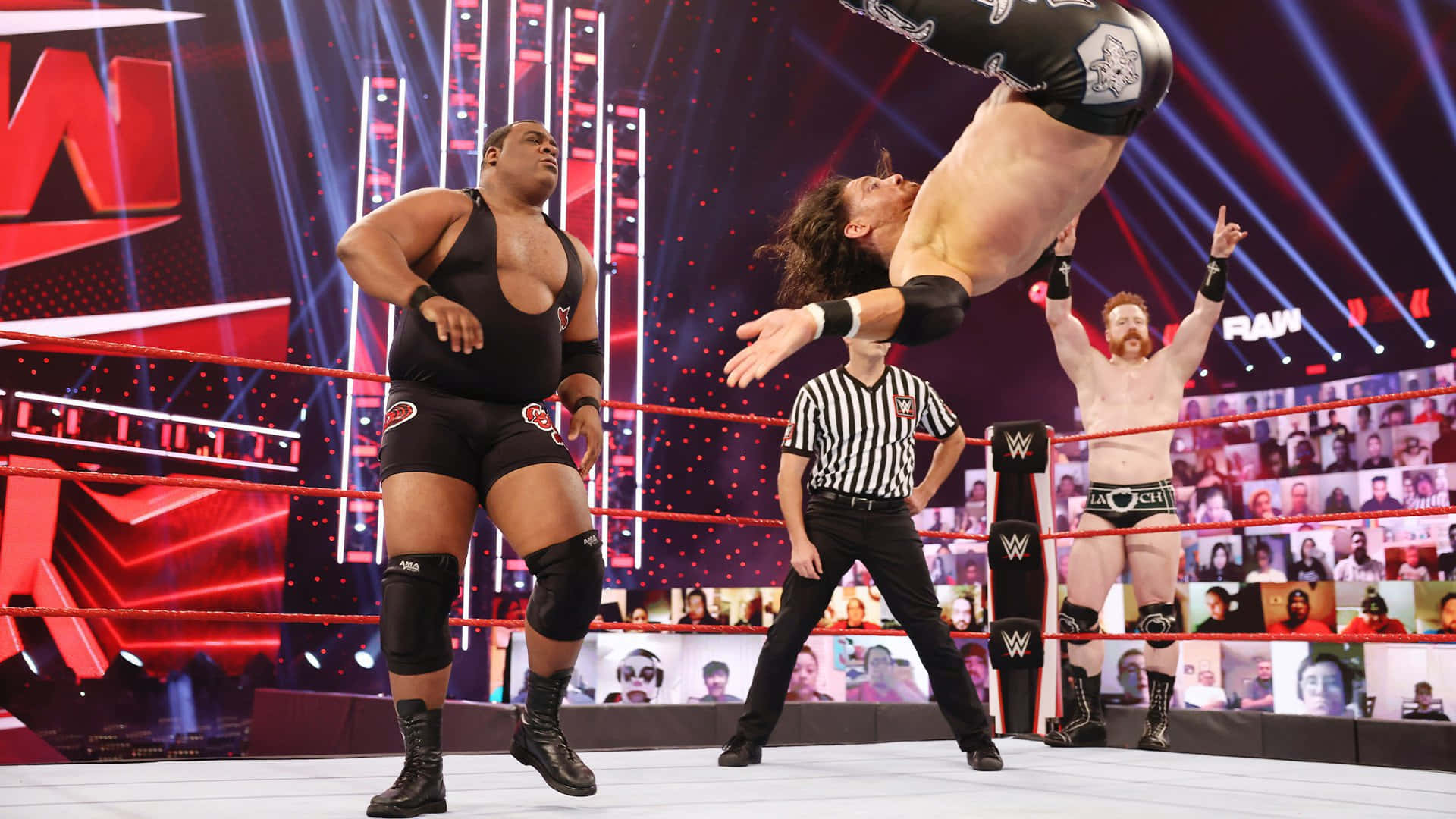 WWE 桌布 壁紙 — 一名摔角手在WWE比賽中高高躍起，他的對手在旁觀看，裁判在下方觀察。