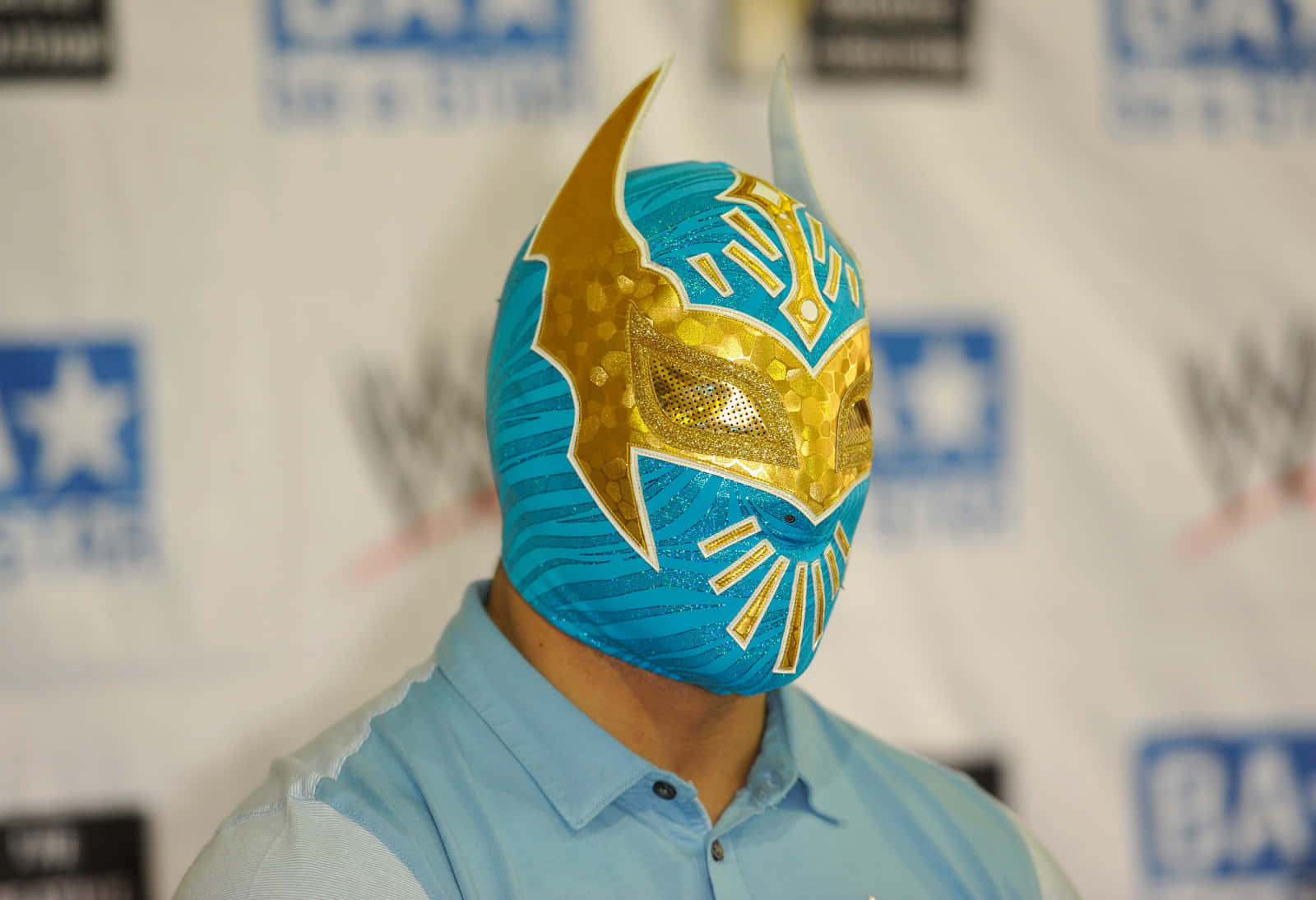 WWE 桌布 壁紙 — 一名摔角手在WWE活動中佩戴鮮豔的藍色和金色自由摔角面具，帶有尖銳的角和複雜的圖案。