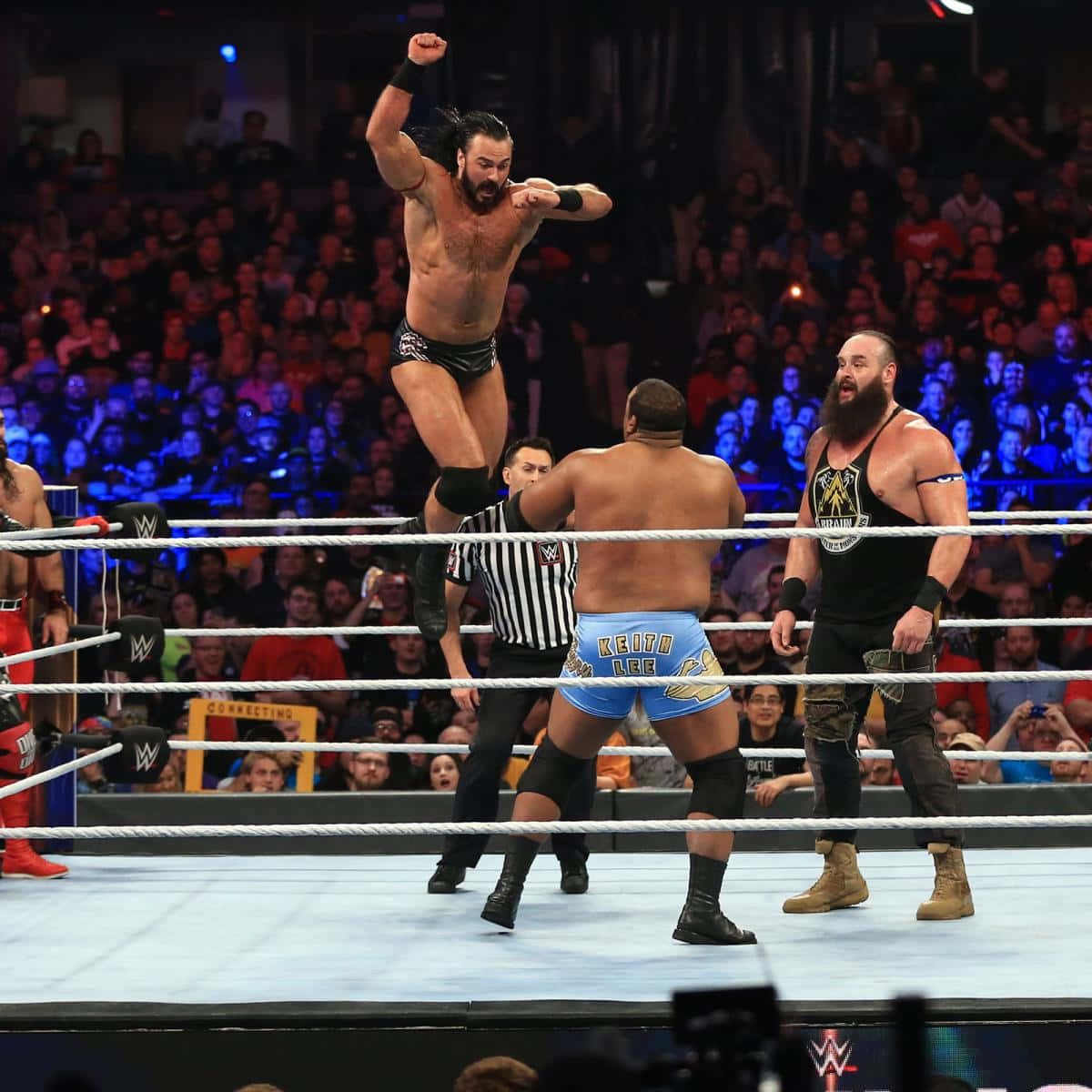 WWE 桌布 壁紙 — 一名摔角手在擂台上方高高躍起，他的對手和裁判在場館燈光下於下方觀看。