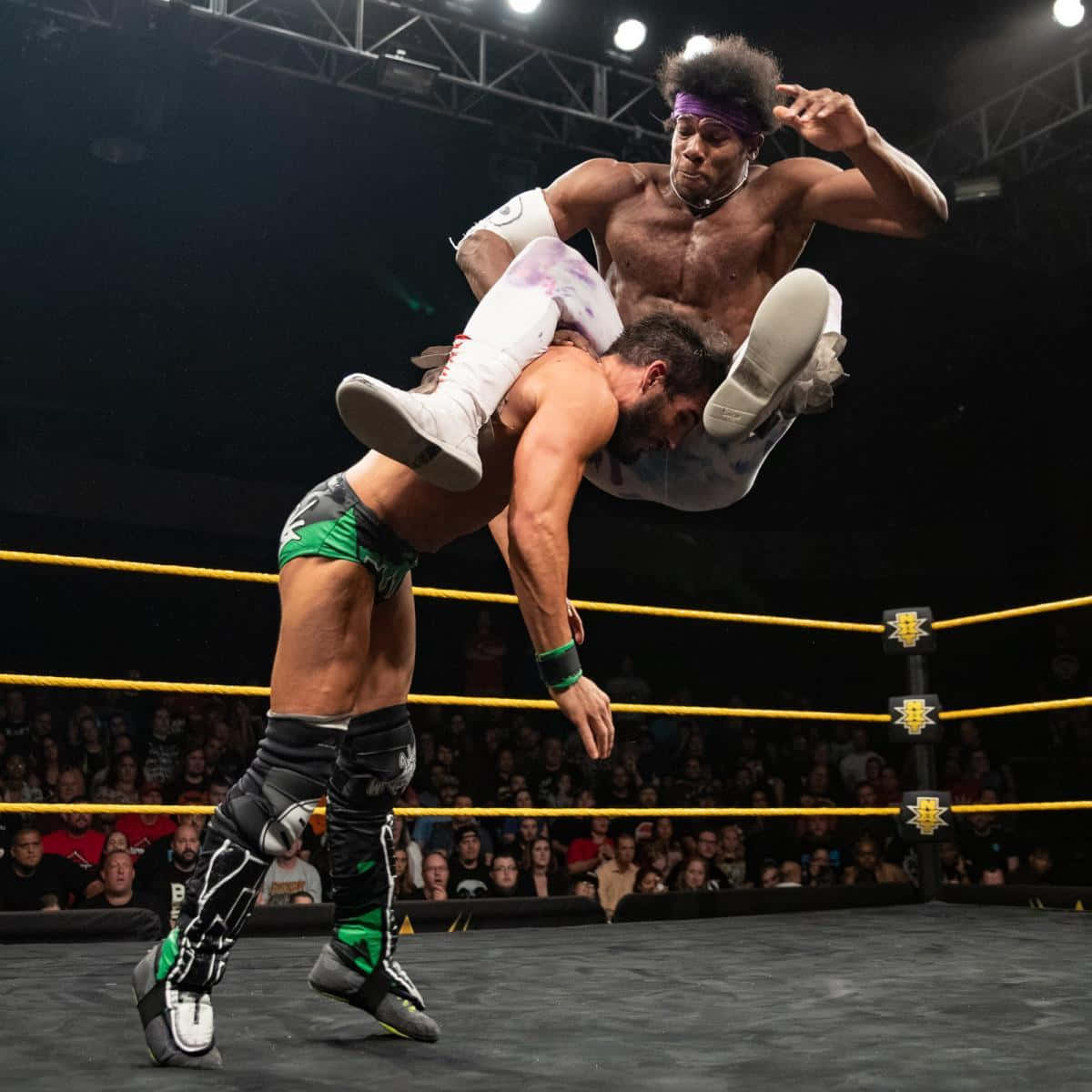 WWE 桌布 壁紙 — 一名摔角手在明亮的場館燈光下，將對手高高舉起，準備施展戲劇性的空中招式。
