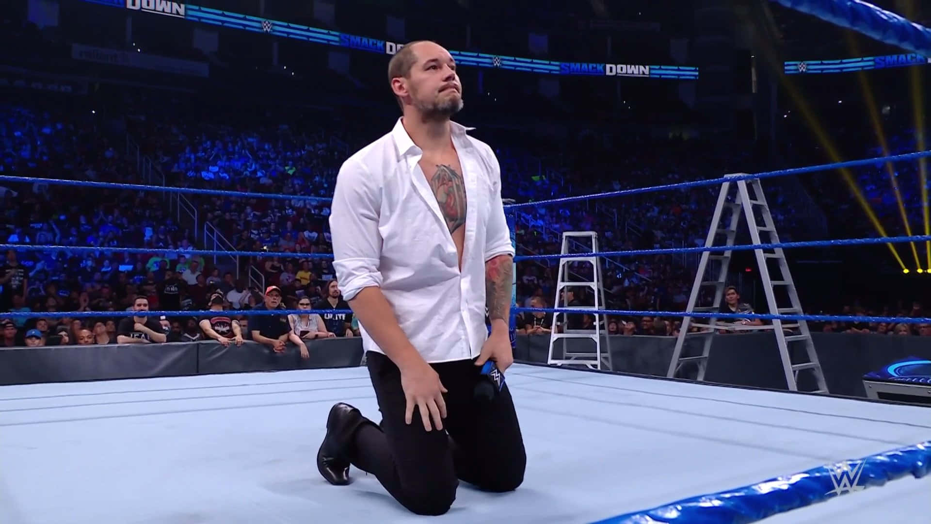 WWE 桌布 壁紙 — 一名摔角手在明亮的場館燈光下跪在WWE擂台上，觀眾正在觀看。