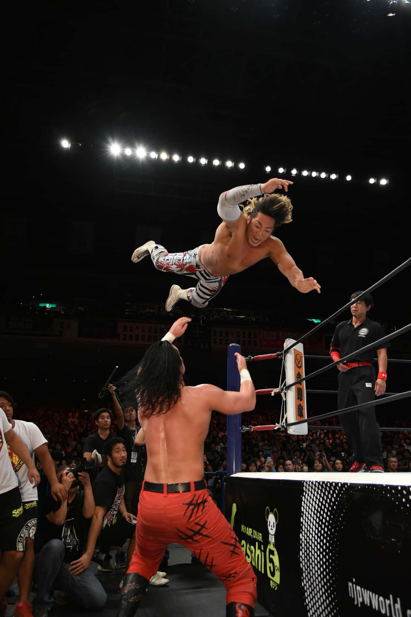 Hiroshi Tanahashi 桌布 壁紙 — 一名摔角手在燈光明亮的擂台上躍起，朝對手飛撲，下方粉絲歡呼。