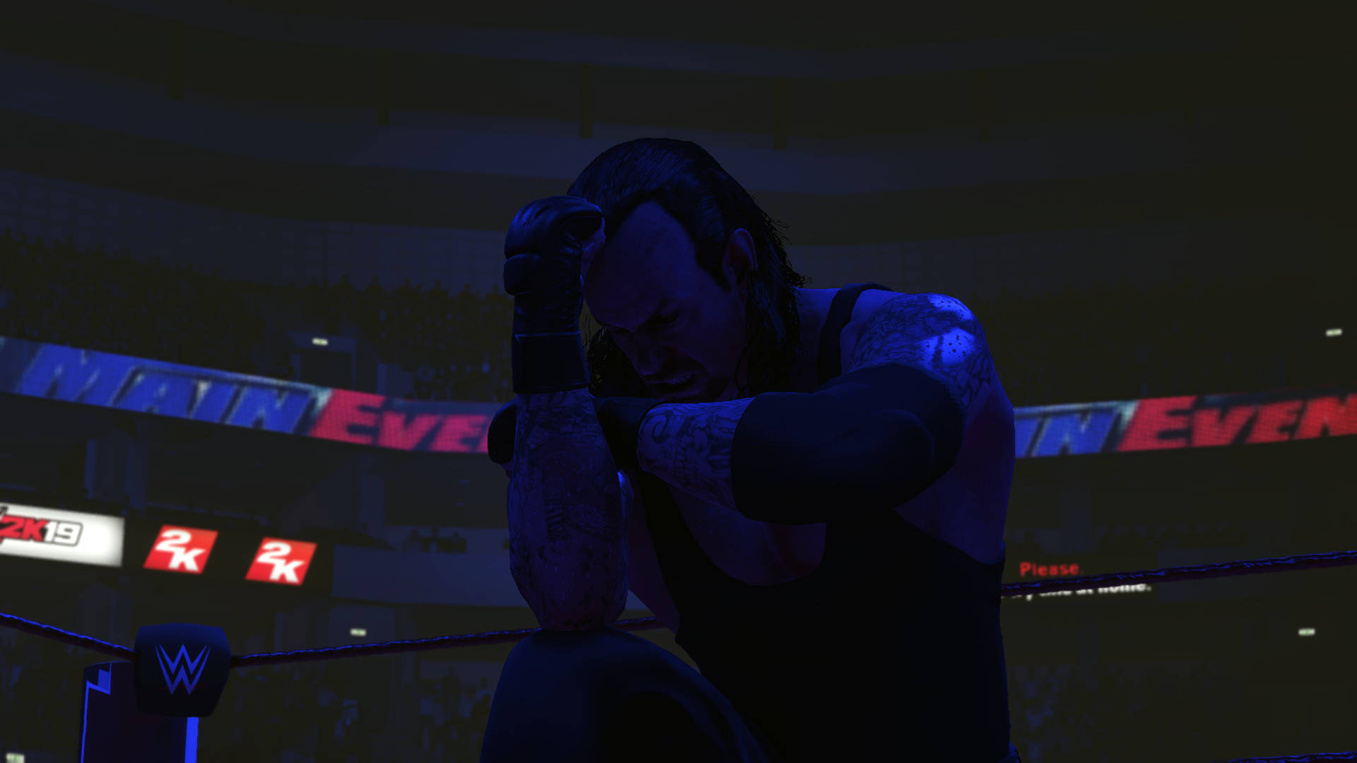Undertaker 桌布 壁紙 — 一名摔角手在黑暗的擂台上，在藍色場館燈光下痛苦地跪著，身後有『MAIN EVENT』的橫幅在發光。