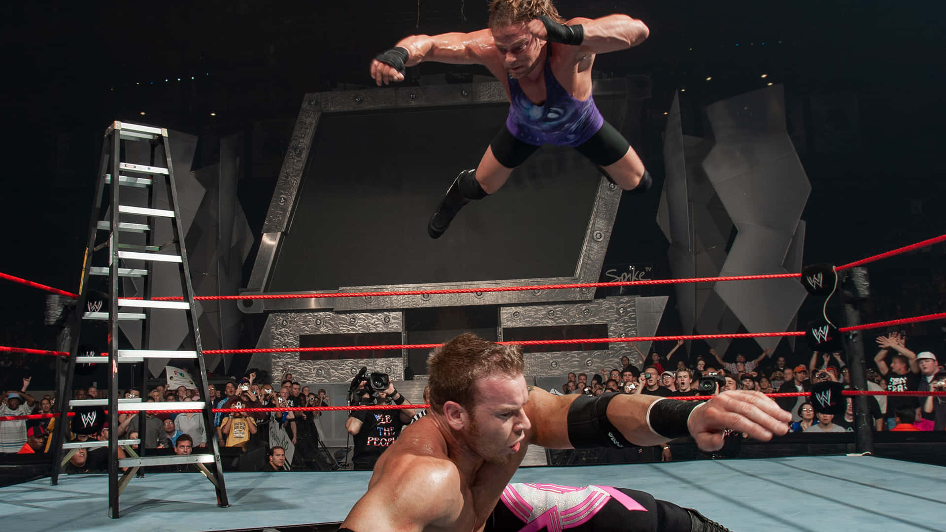 WWE 桌布 壁紙 — 一名摔角手從梯子上跳向WWE擂台中的對手，台下觀眾歡呼。