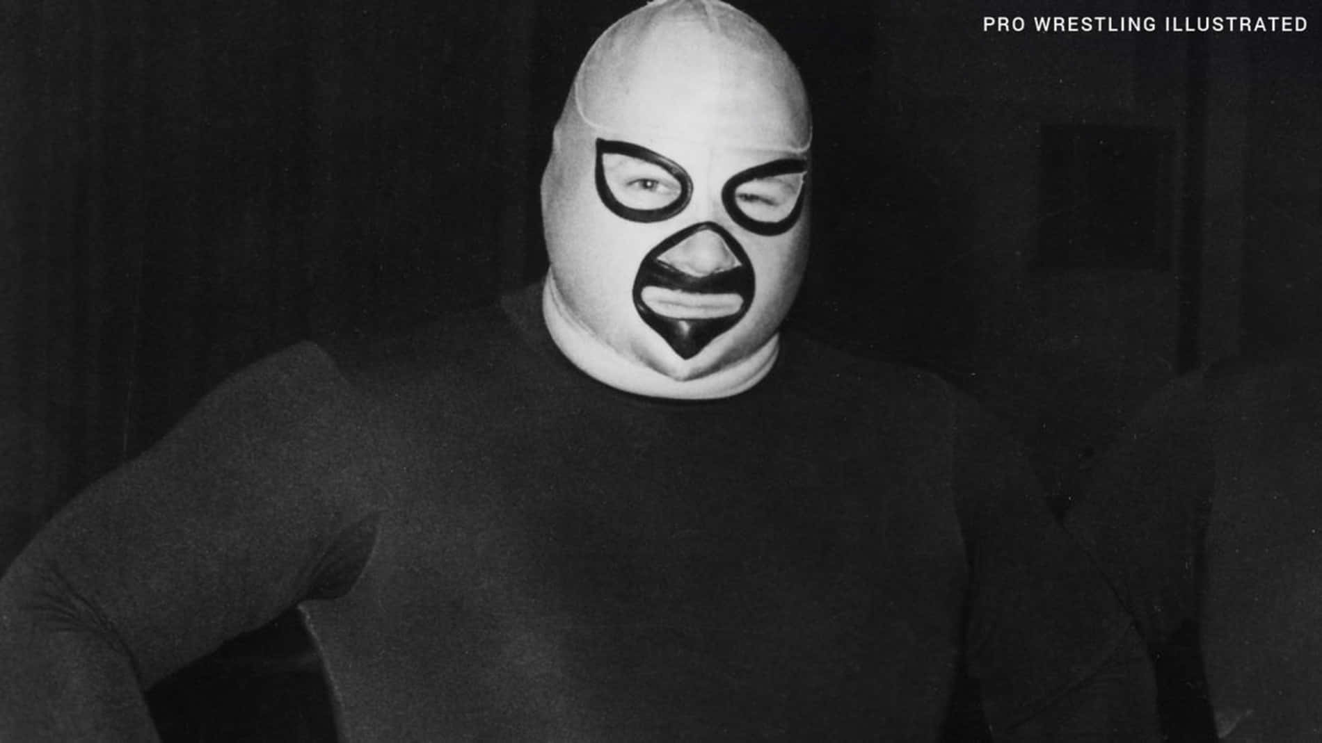 WWE 桌布 壁紙 — 一名摔角手戴著白色面具，上面有醒目的黑色面部標記，在昏暗的房間裡自信地擺姿勢。