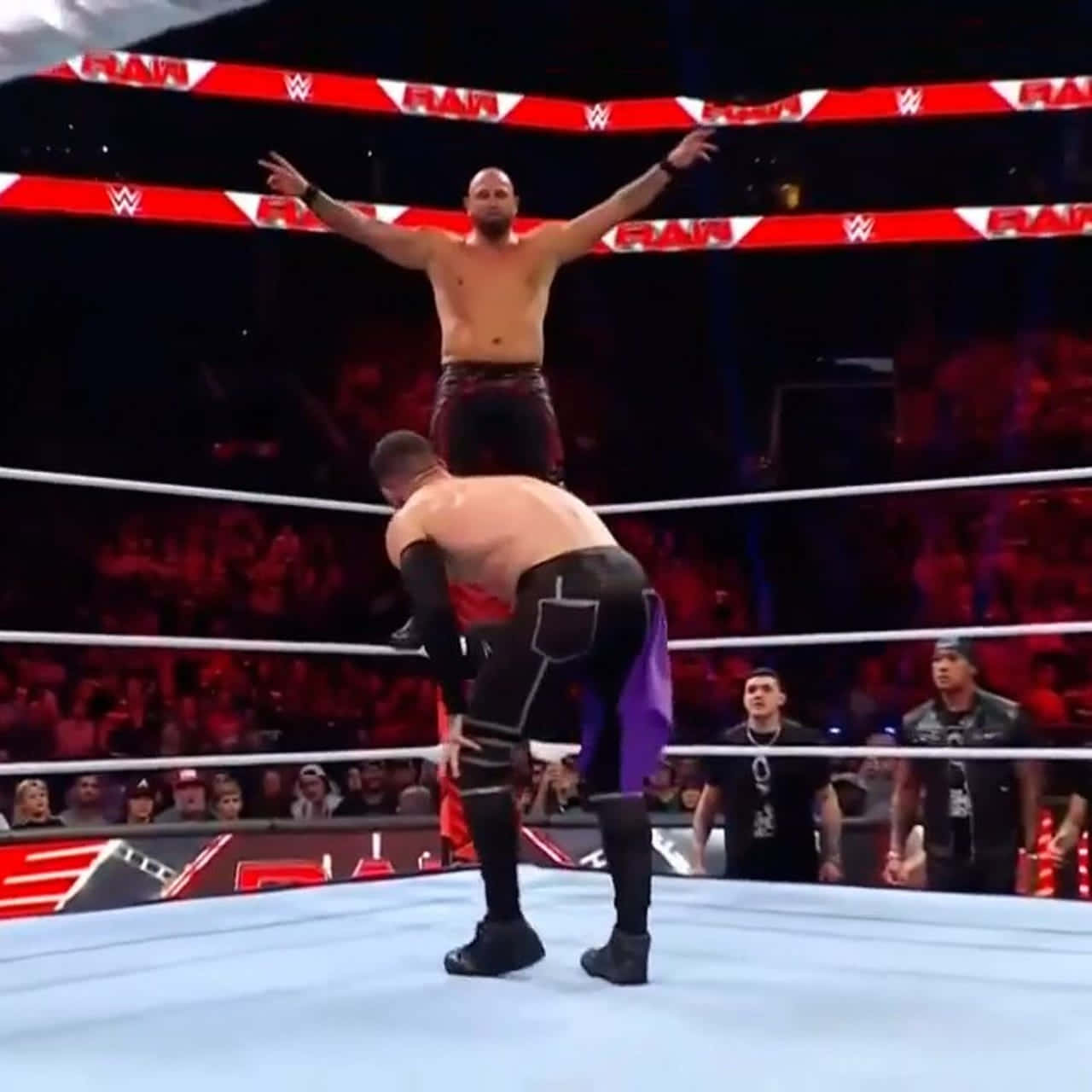 WWE 桌布 壁紙 — 一名摔角手站在WWE擂台上另一人之上，高舉雙臂，而群眾在下方觀看。