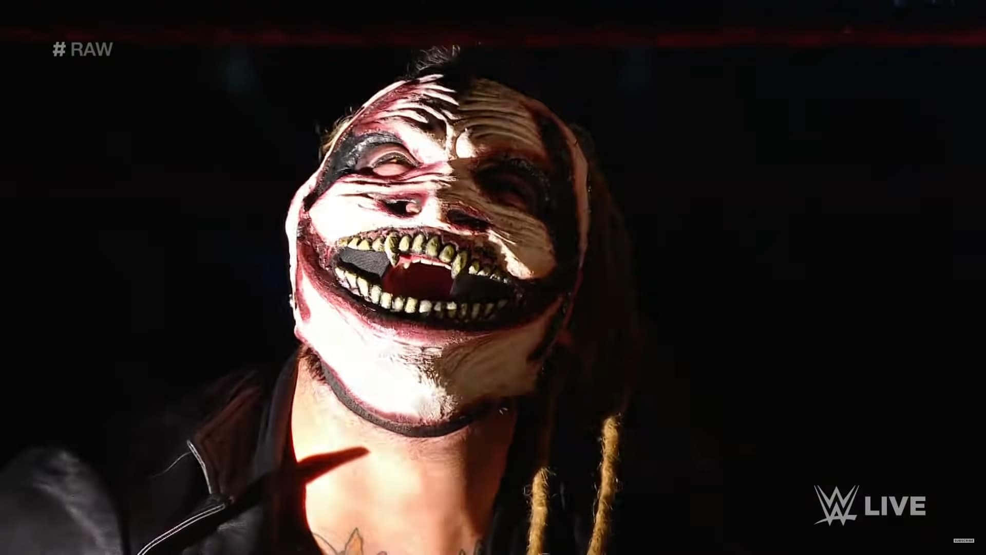 WWE 桌布 壁紙 — 一名摔角手臉上塗著怪誕的顏料，在黑暗背景的明亮舞台燈光下狂笑。