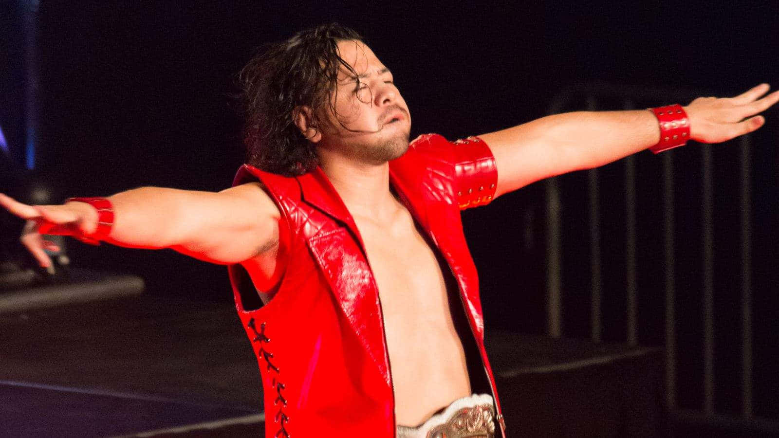 WWE 桌布 壁紙 — 一名摔角手身穿閃亮紅色背心和冠軍腰帶，在舞台燈光下張開雙臂擺出勝利姿勢。