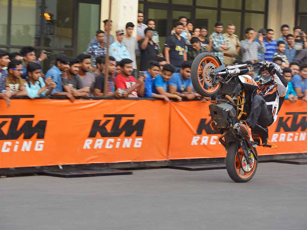 KTM 摩托車 桌布 壁紙 — 一名摩托車手在賽車活動中，在人群面前駕駛橙色KTM摩托車表演翹前輪。