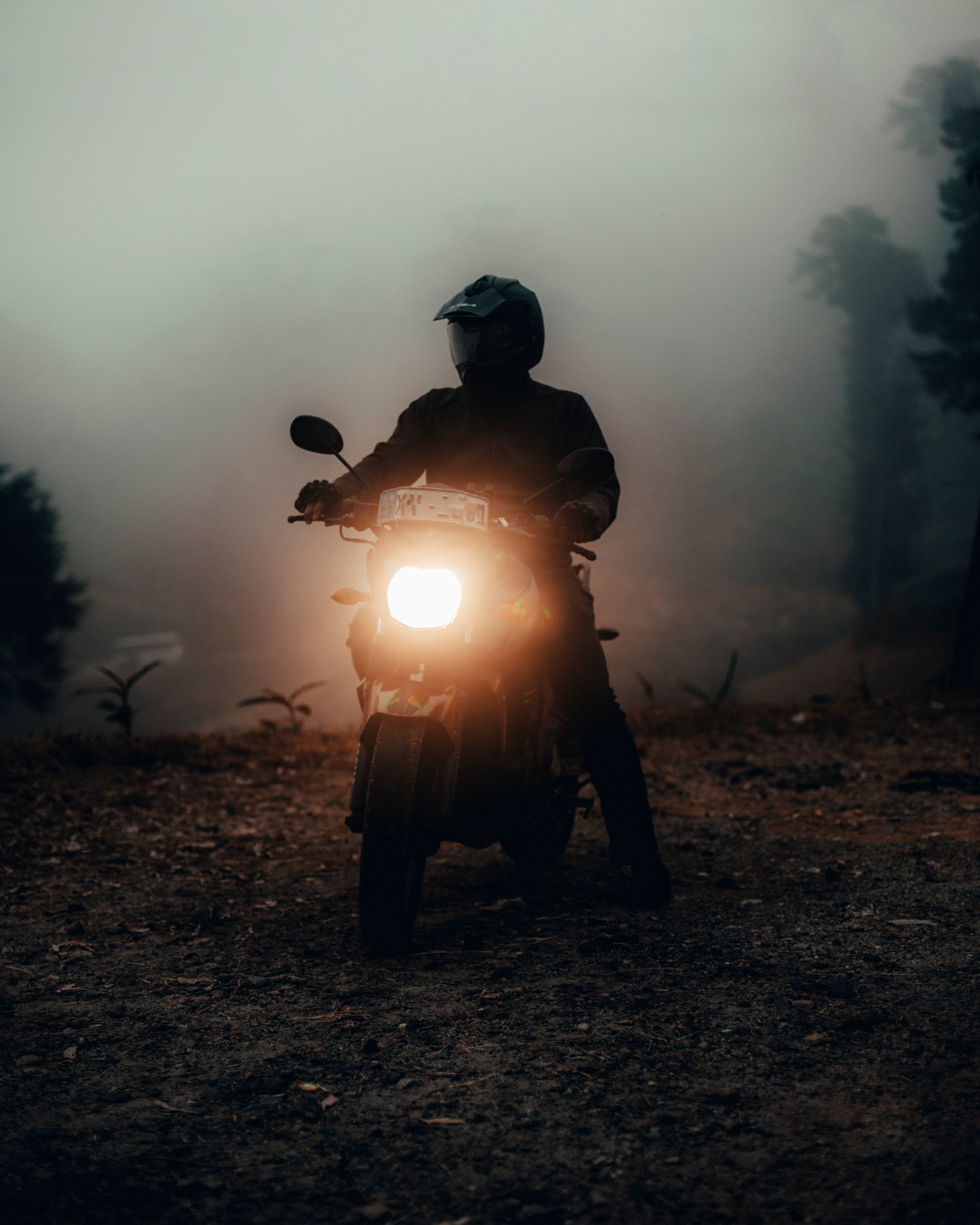 Bike Rider 桌布 壁紙 — 一名摩托車手的剪影在濃霧中騎行，明亮的車頭燈劃破霧氣瀰漫的森林小徑。