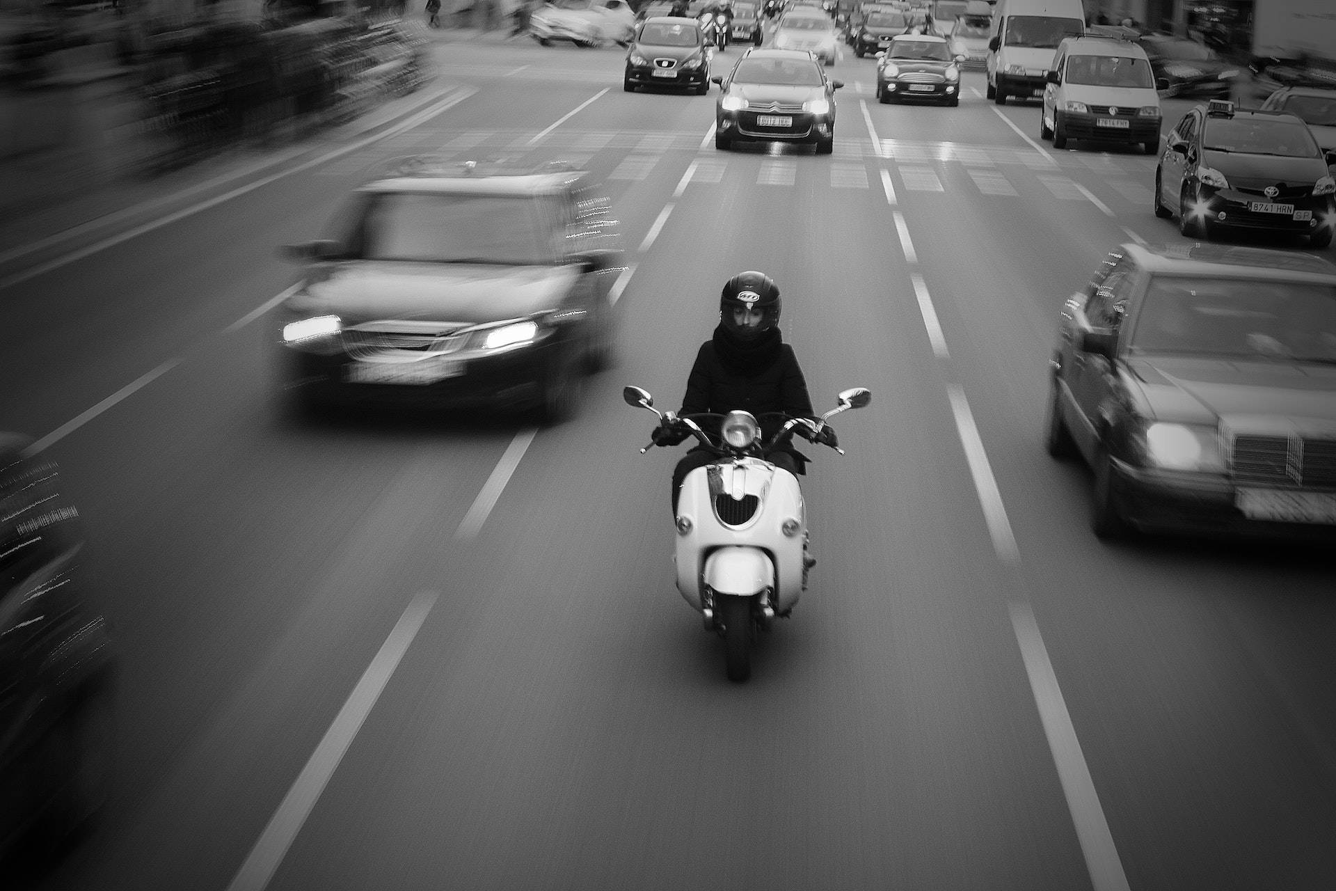Speed 桌布 壁紙 — 一名摩托車騎士騎著白色速克達穿過繁忙的街道，背景有模糊的汽車，以黑白呈現。