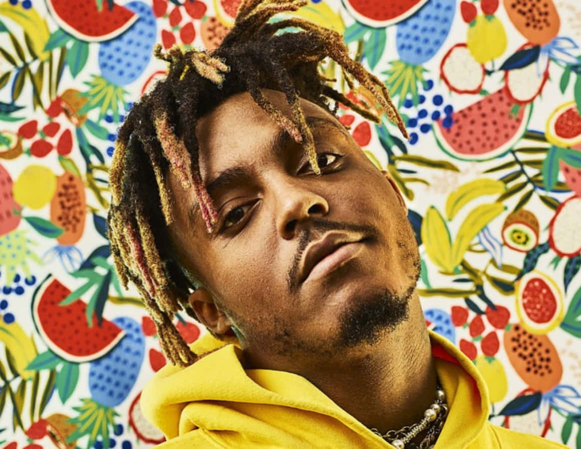 男子穿著黃色連帽衫，辮子頭，以熱帶水果壁紙為背景。 — Juice Wrld 壁紙