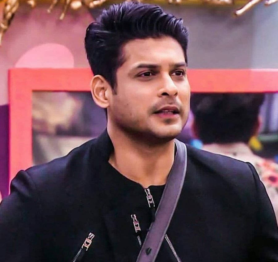 Sidharth Shukla 桌布 壁紙 — 一名擁有時尚黑髮的男子，在色彩繽紛的模糊背景前，穿著一件胸前有灰色帶子的黑色拉鍊外套。