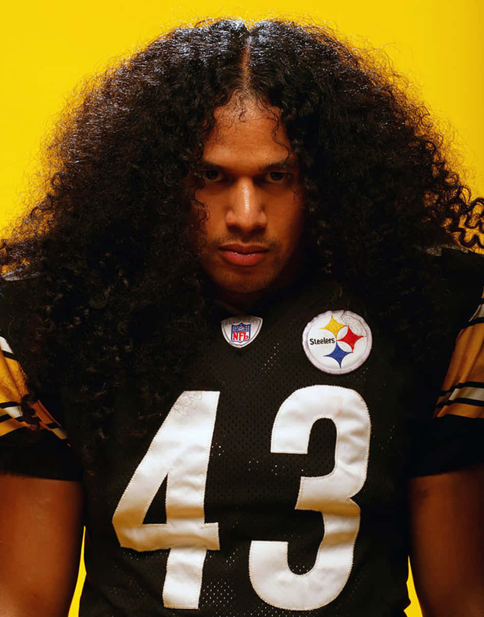 Troy Polamalu 桌布 壁紙 — 一名擁有濃密捲髮的足球員，身穿黑色鋼人隊球衣，在明亮的黃色背景下凝視著。