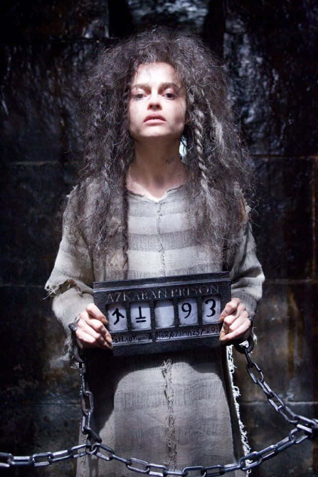 Death Eaters 桌布 壁紙 — 一名擁有狂野灰髮的女人被鎖鏈鎖在黑暗的石牢中，手持囚犯號碼牌。