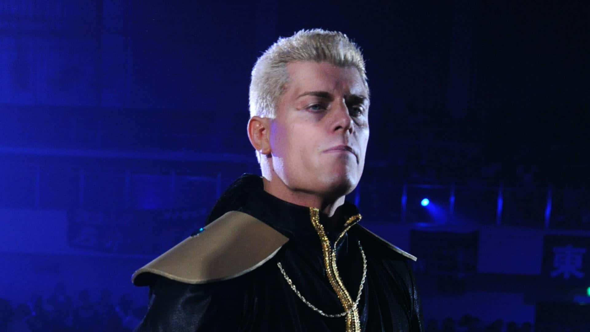 WWE Desktop 桌布 壁紙 — 一名擁有鉑金色頭髮和金色鏈條的摔角手在藍色競技場燈光下凝視著。