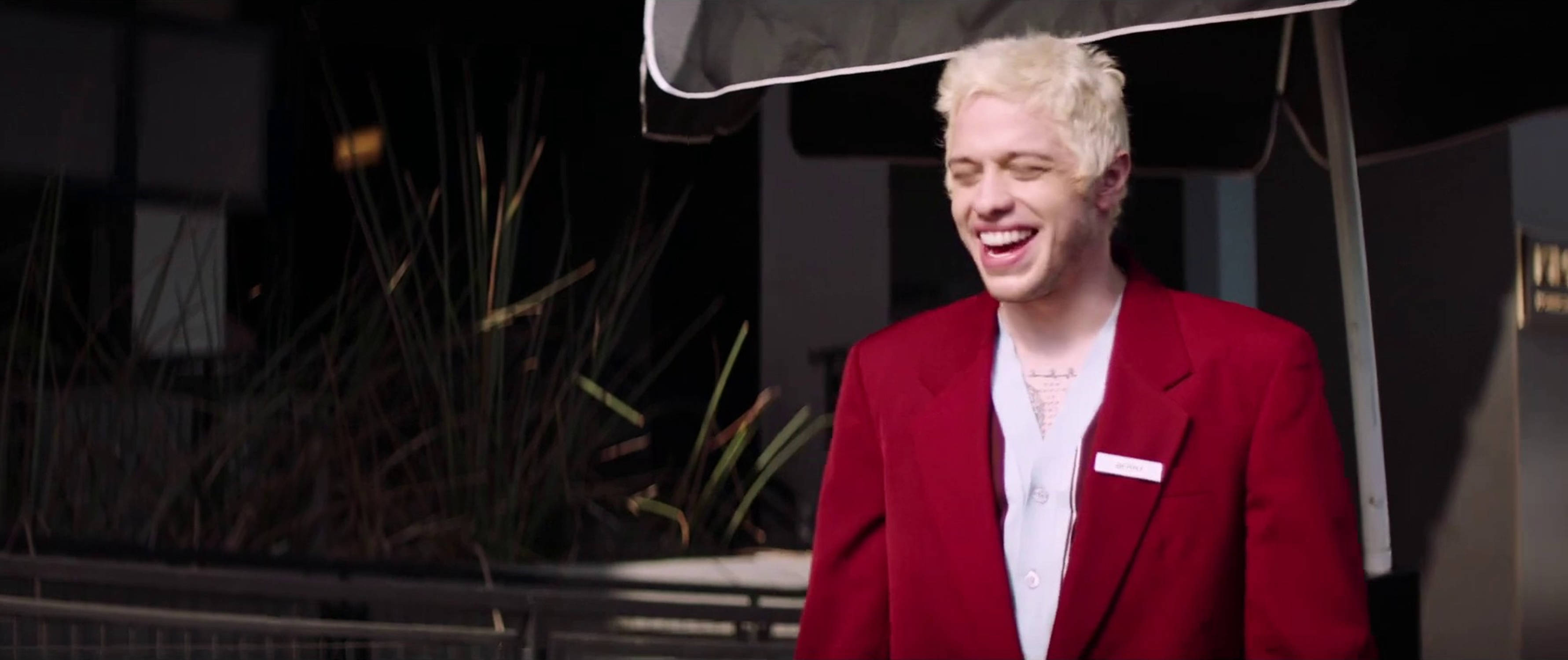 Pete Davidson 桌布 壁紙 — 一名擁有鉑金色頭髮的男子，在夜間戶外遮陽篷下，穿著鮮紅色西裝外套，開懷大笑。
