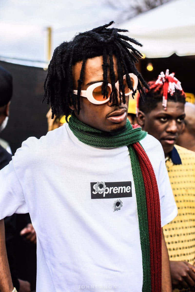 Playboi Carti HD 桌布 壁紙 — 一名擁有長黑色辮子和白色太陽眼鏡的男子，穿著白色Supreme T恤和綠紅圍巾，站在戶外。