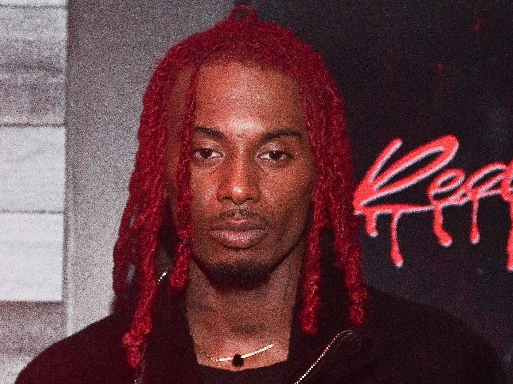 Carti 桌布 壁紙 — 一名擁有鮮紅色辮子髮型的男子在帶有紅色塗鴉的黑暗背景下專注地凝視著鏡頭。