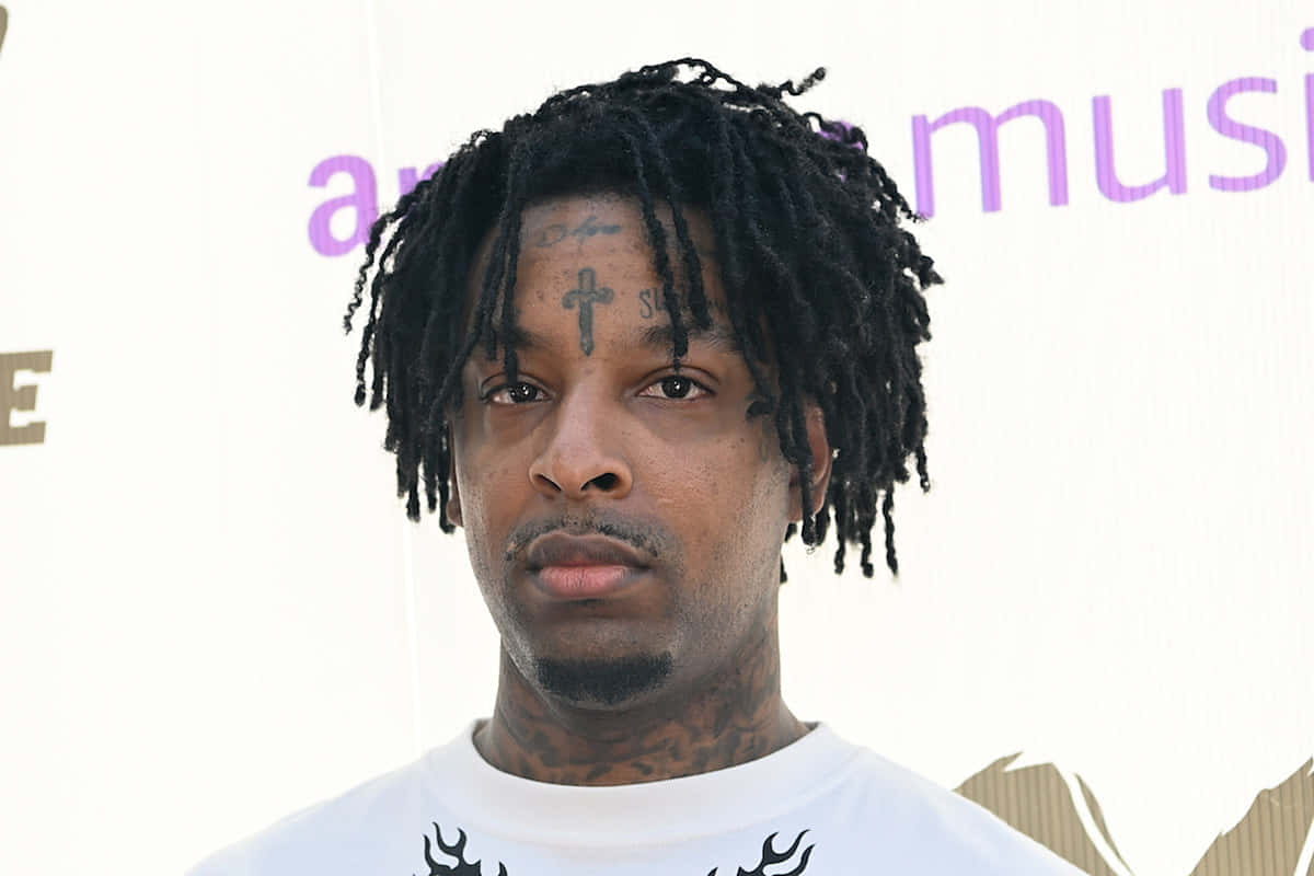 21 Savage 桌布 壁紙 — 一名擁有黑色辮子頭和面部刺青的男子特寫肖像，背景為白色並帶有紫色文字。