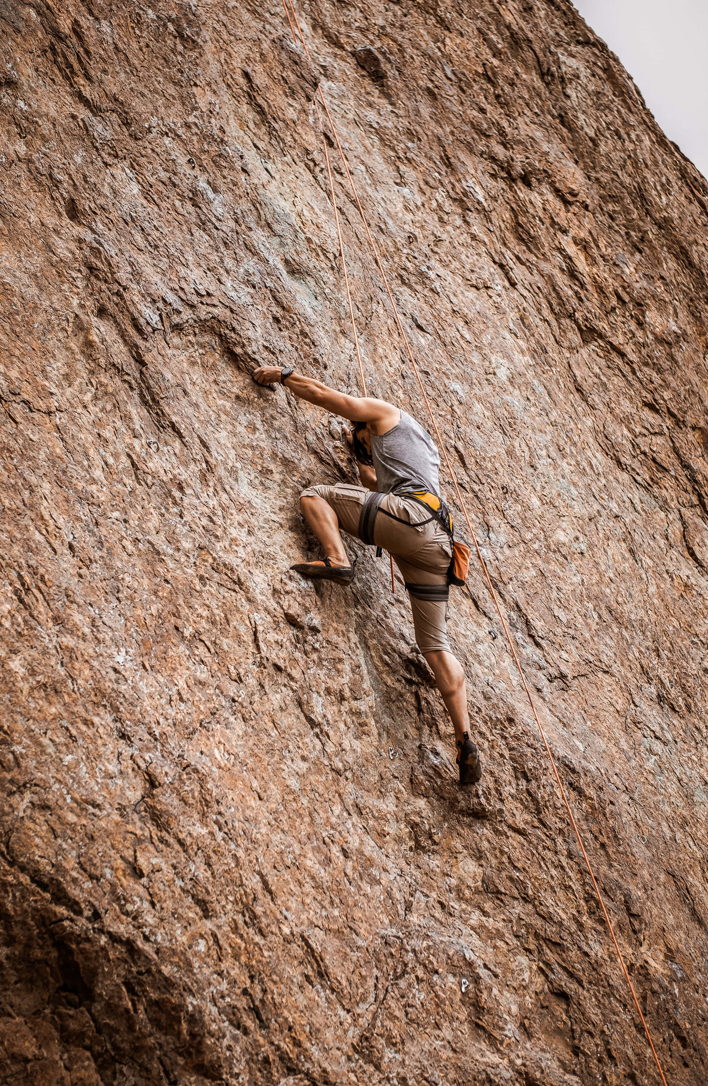 Climbing 桌布 壁紙 — 一名攀岩者在多雲的天空下，專注地攀登崎嶇的棕色岩壁。