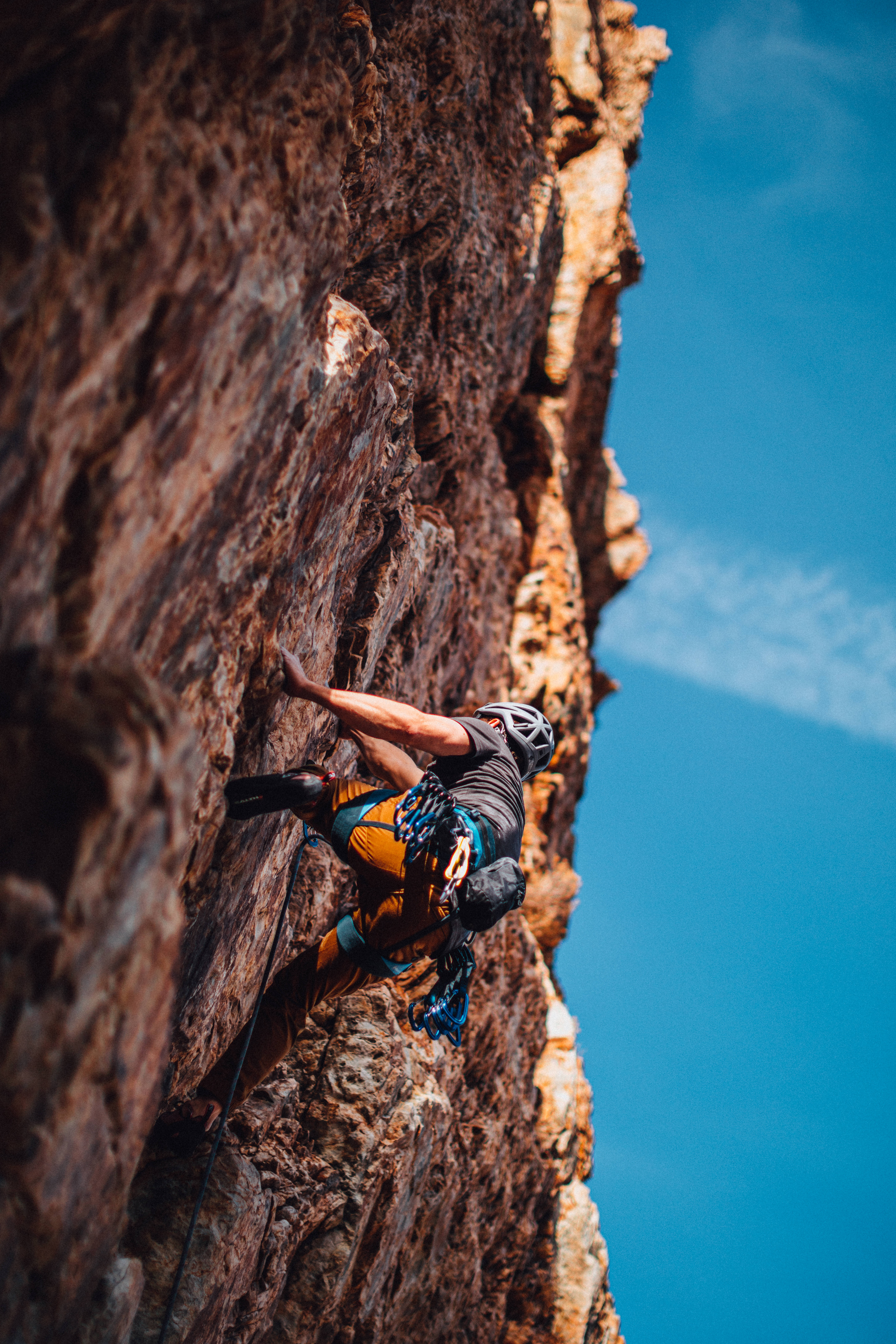 Rock Climbing 桌布 壁紙 — 一名攀岩者在晴朗藍天與單薄雲朵下攀爬崎嶇的紅褐色懸崖。