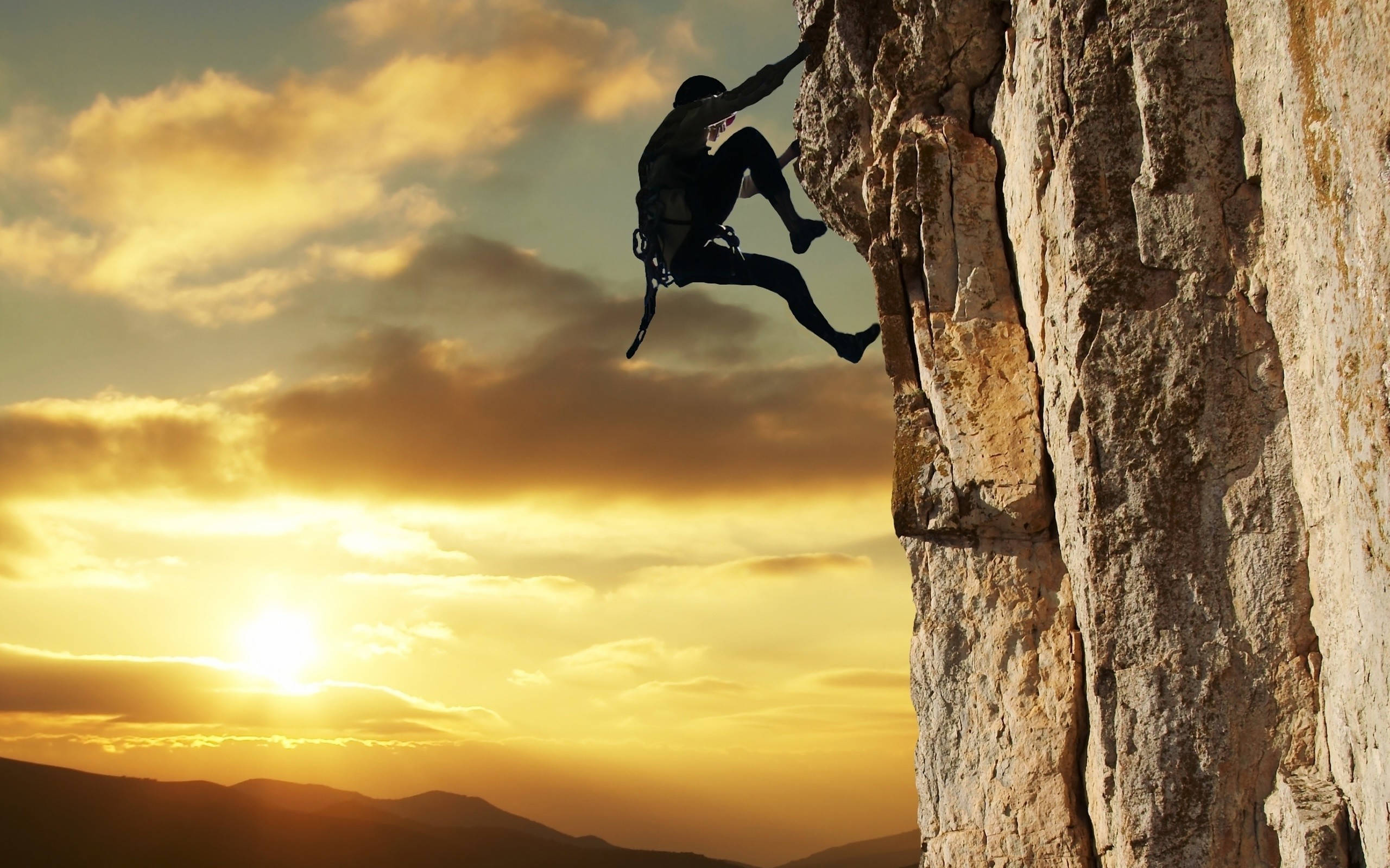 Climbing 桌布 壁紙 — 一名攀岩者正在攀爬崎嶇的懸崖面，背景是金色夕陽天空和戲劇性的雲彩。